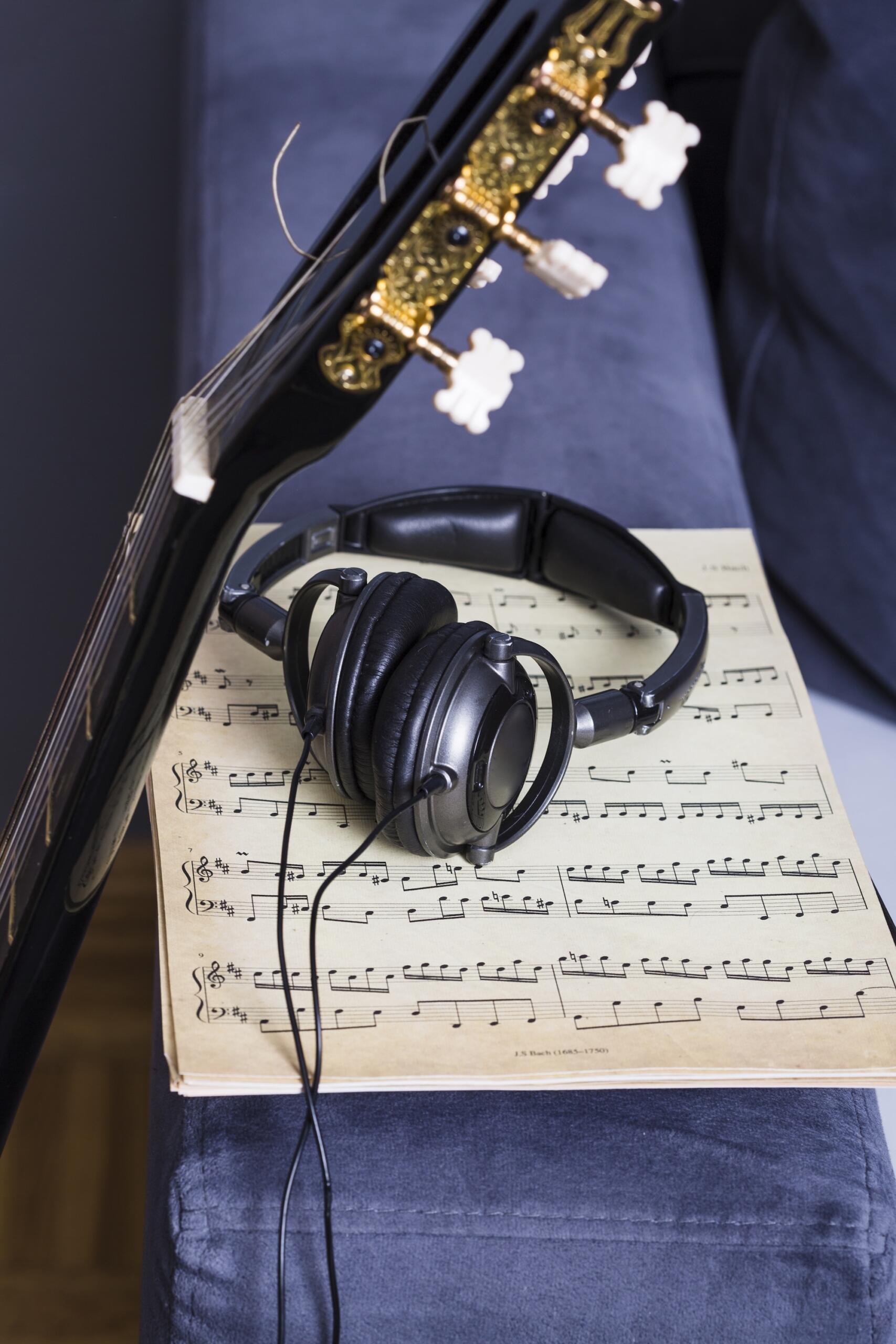 Une guitare est posée le long d'une partition, avec un casque dessus