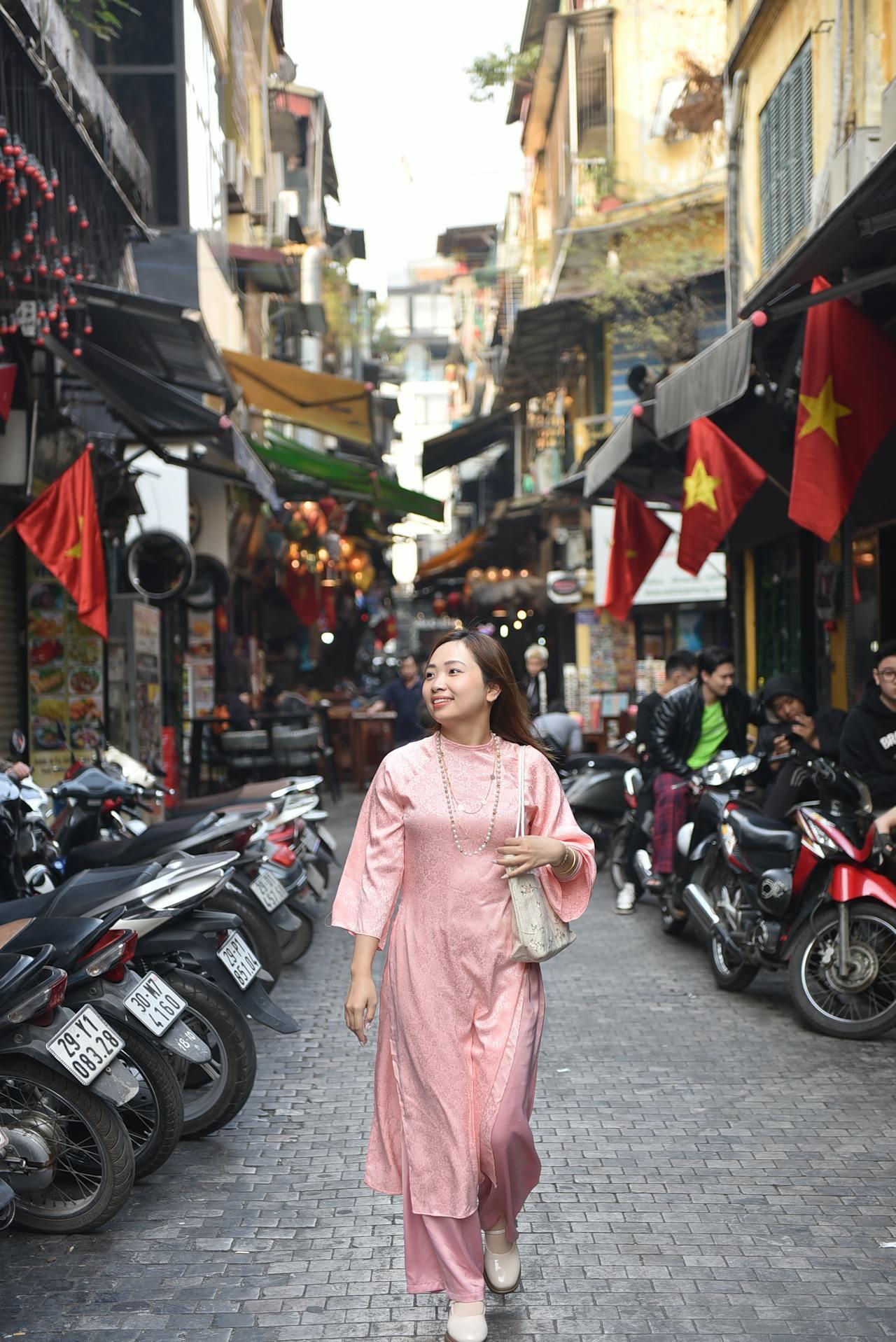 Jeune vietnamienne se promenant dans une rue du Vietnam où des drapeaux du pays sont accrochés de chaque côté. 