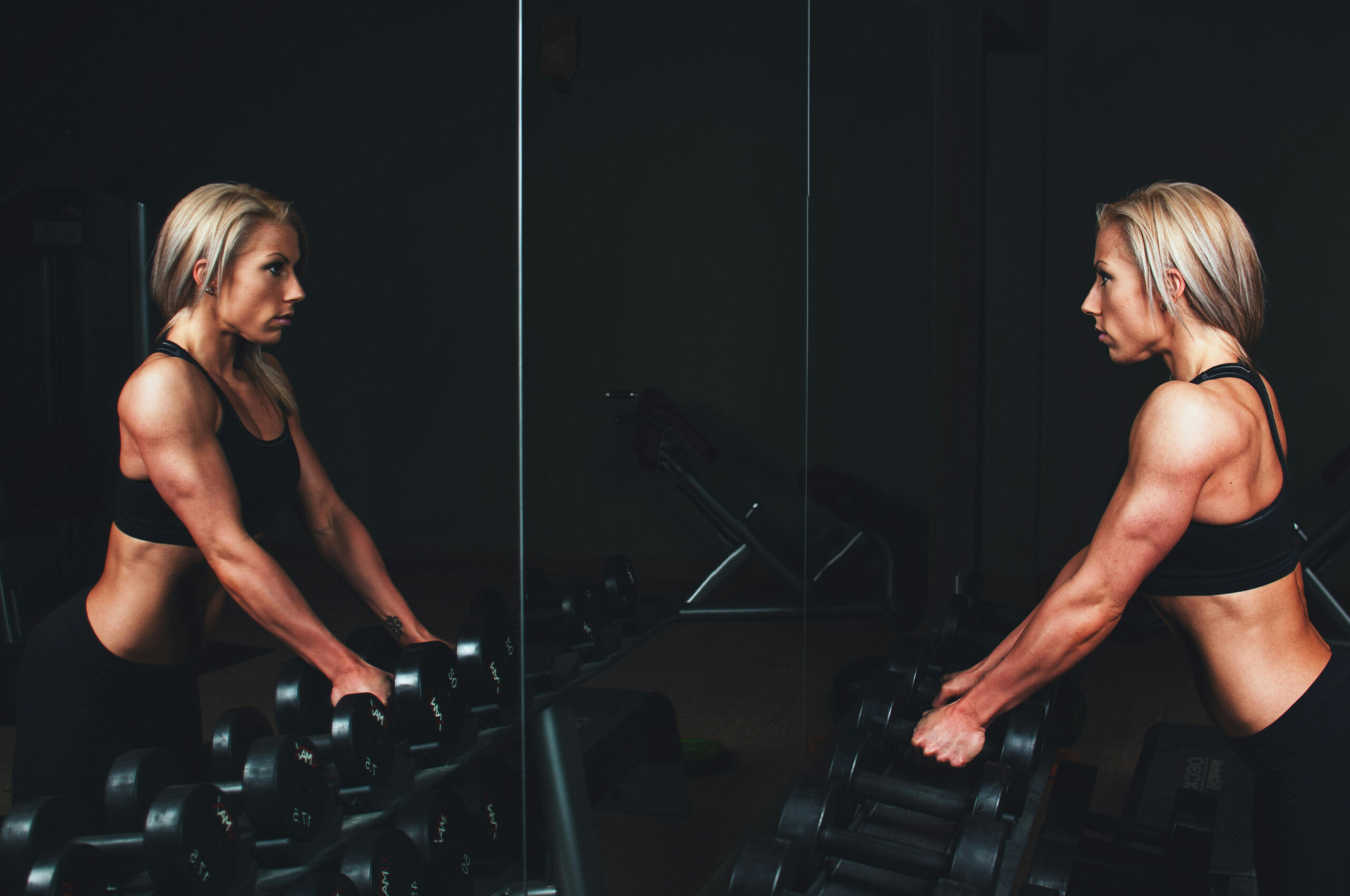 Une sportive face à son reflet dans une salle de sport noire.