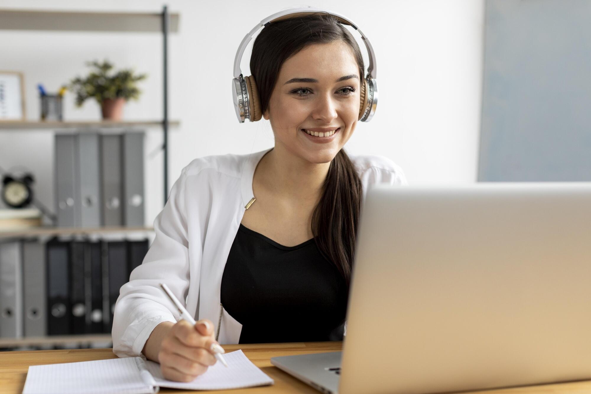 Une femme est devant son ordinateur en train de prendre des notes.