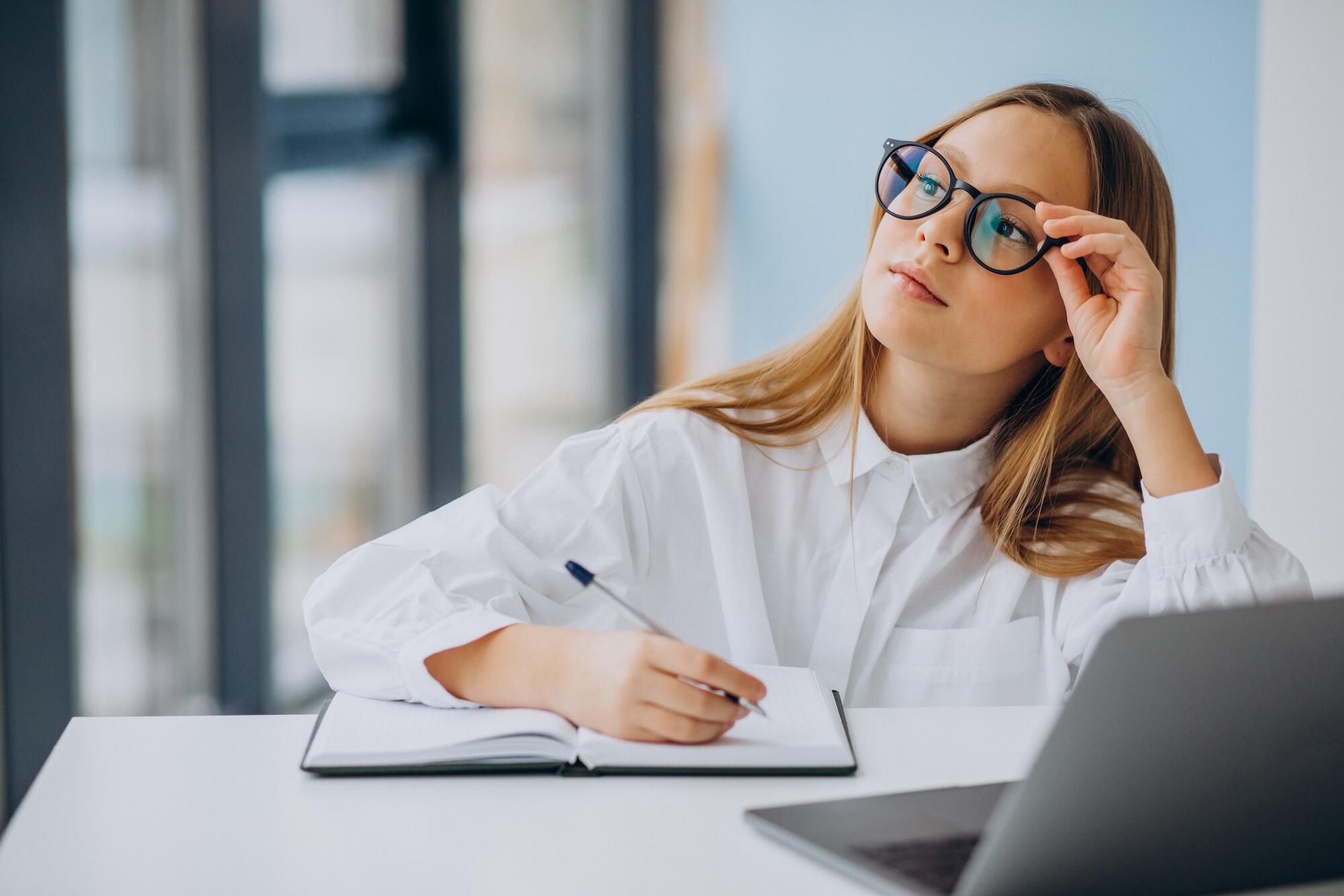 Une jeune femme avec des lunettes est en train d'écrire sur un bureau.