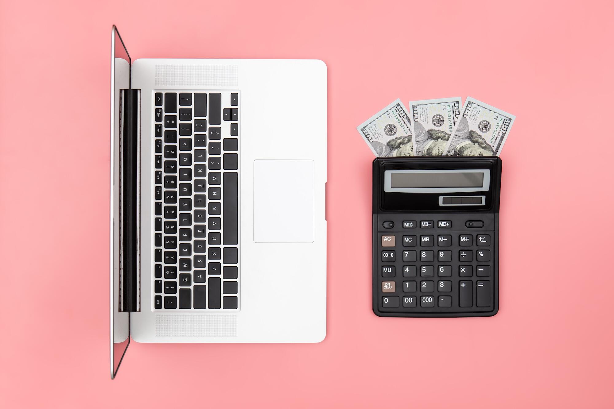 Un ordinateur est posé sur une table à côté d'une calculette et de billets.