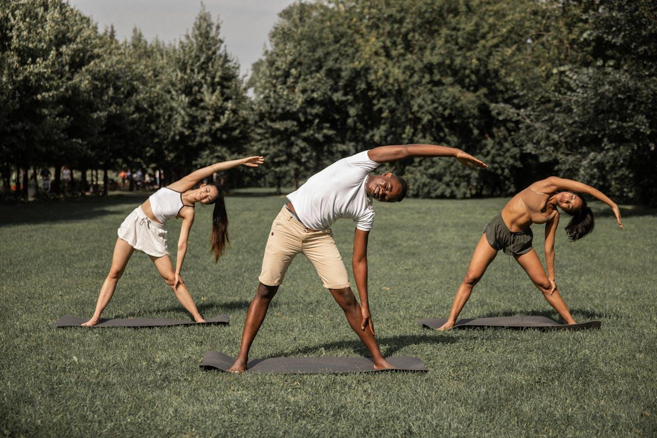 Trois personnes réalisant des flexions de buste debout sur le côté gauche, dans l'herbe.