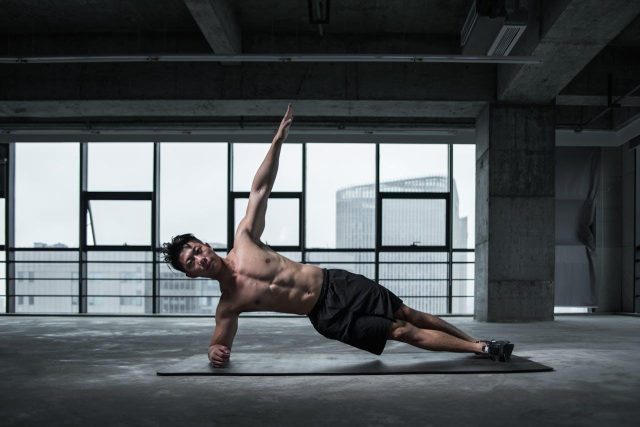 Homme asiatique réalisant un gainage latéral avec un bras en l'air.