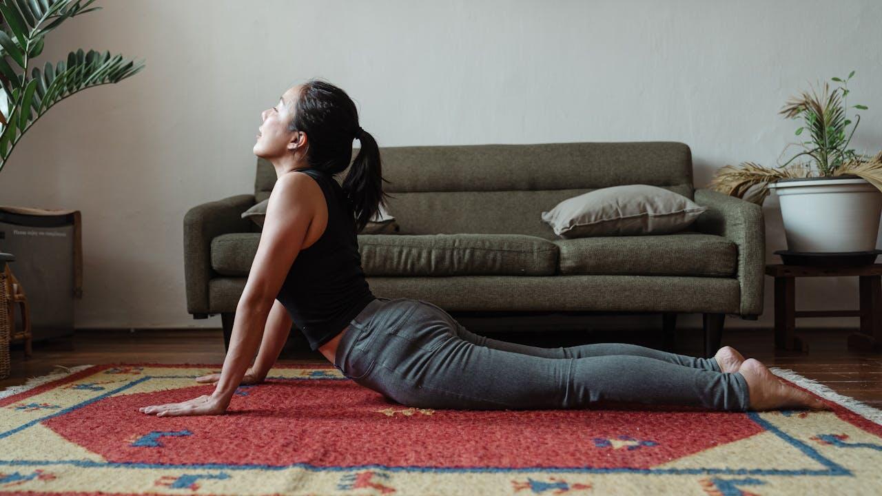 Jeune femme réalisant la posture du cobra sur un tapis chez elle dans son salon.