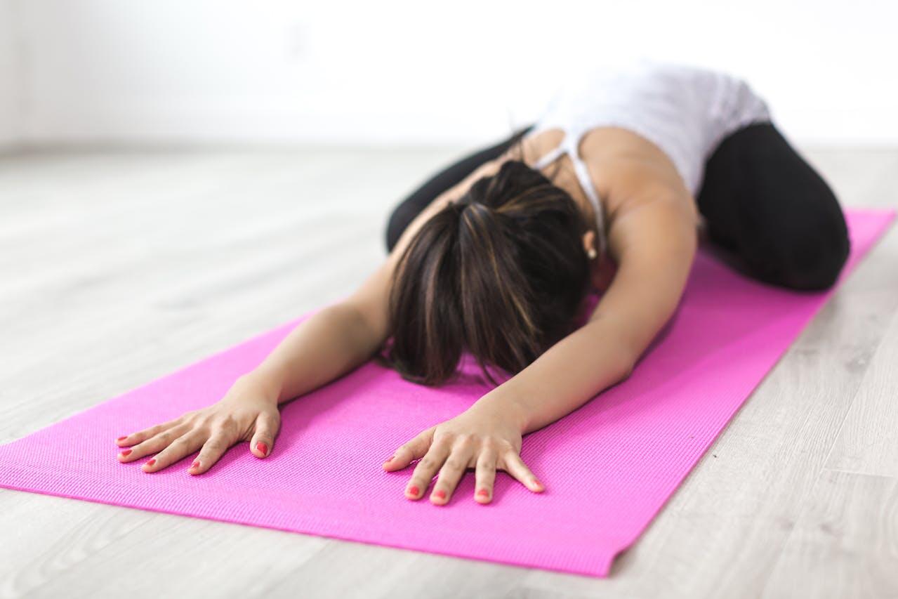 Jeune femme réalisant la posture de l'enfant sur un tapis rose.