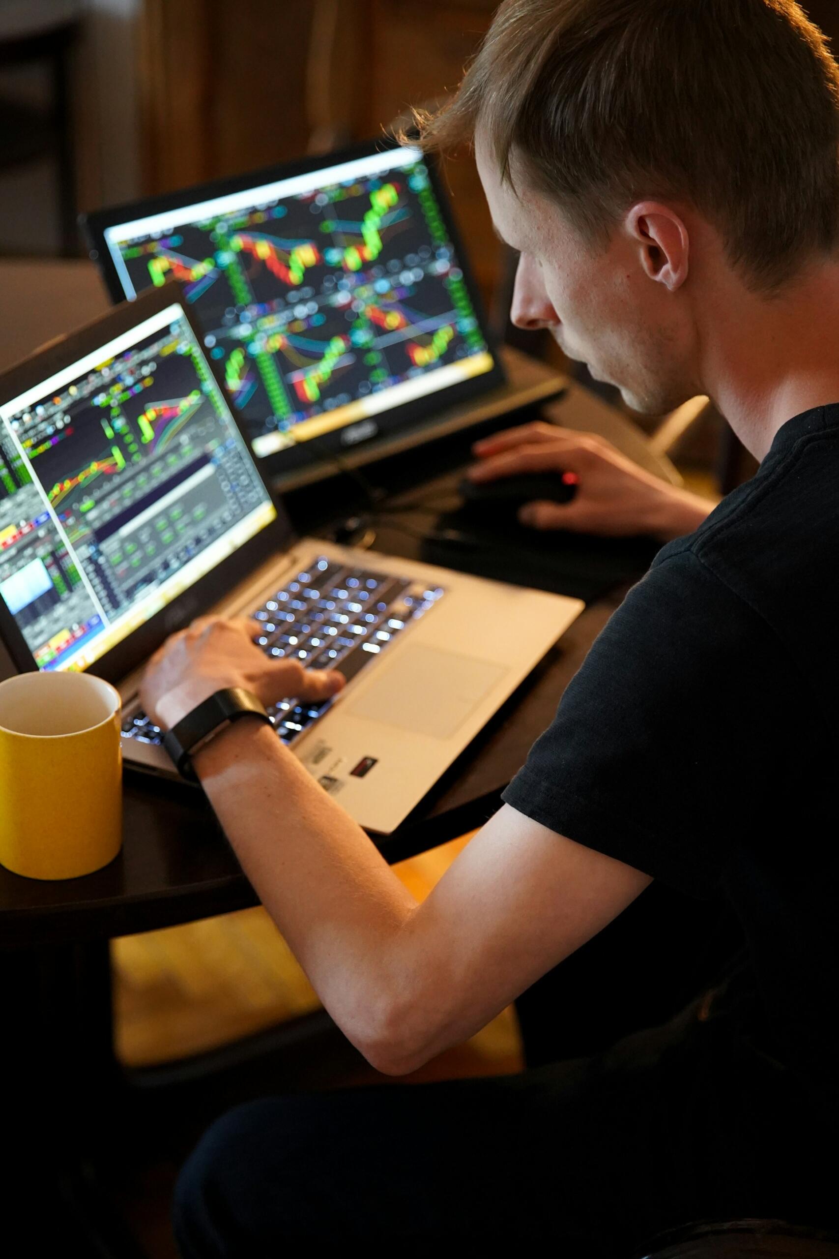 jeune homme devant son ordinateur et ses fiches de trading