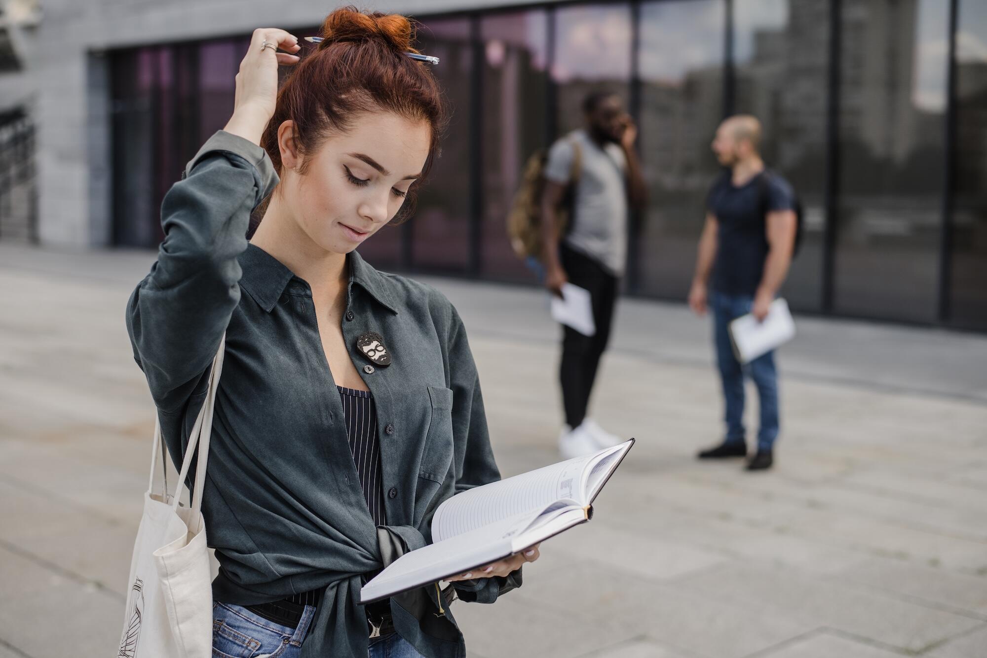 Une jeune étudiante est devant l'université avec un carnet.