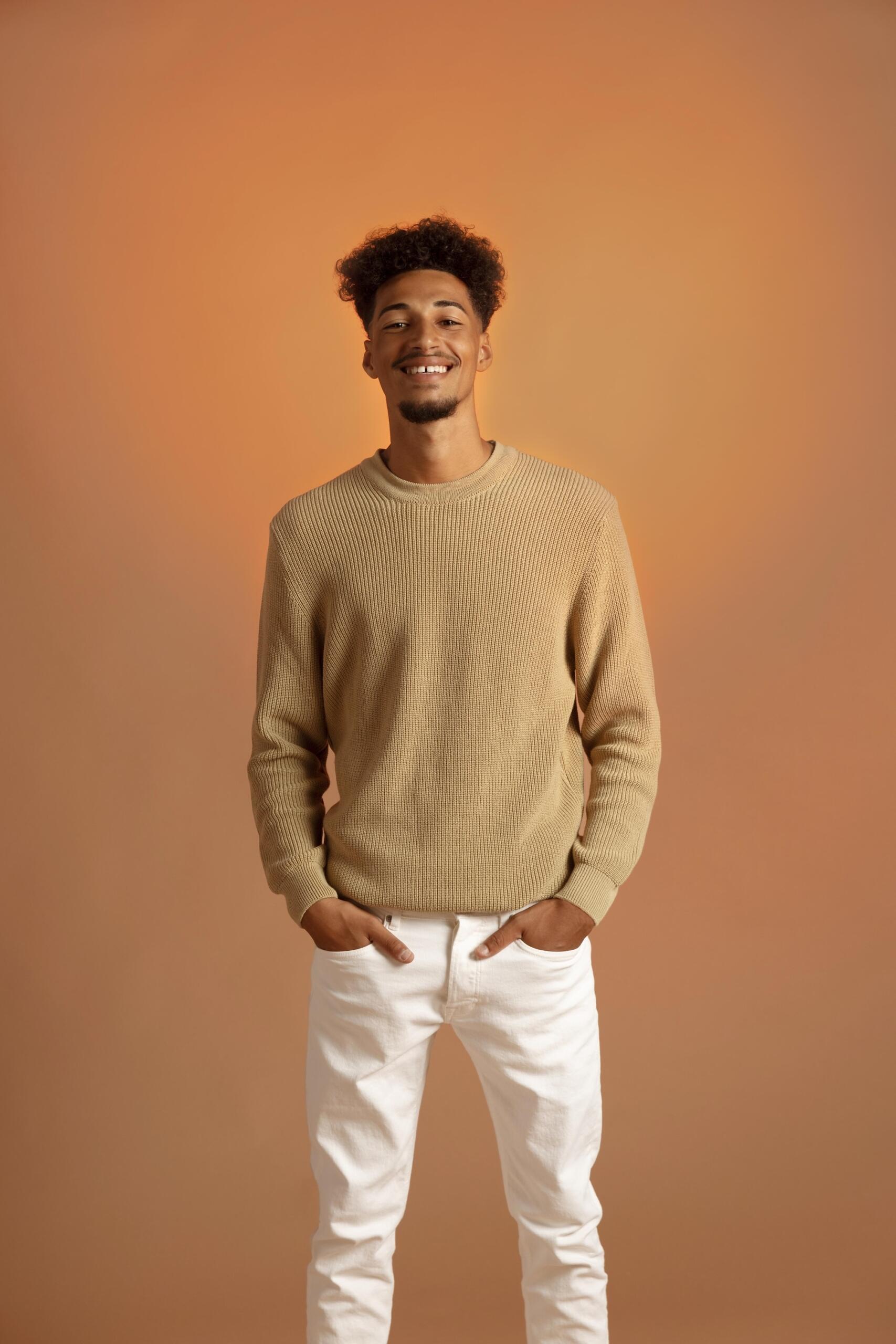 Un jeune homme porte un pull et un pantalon blanc