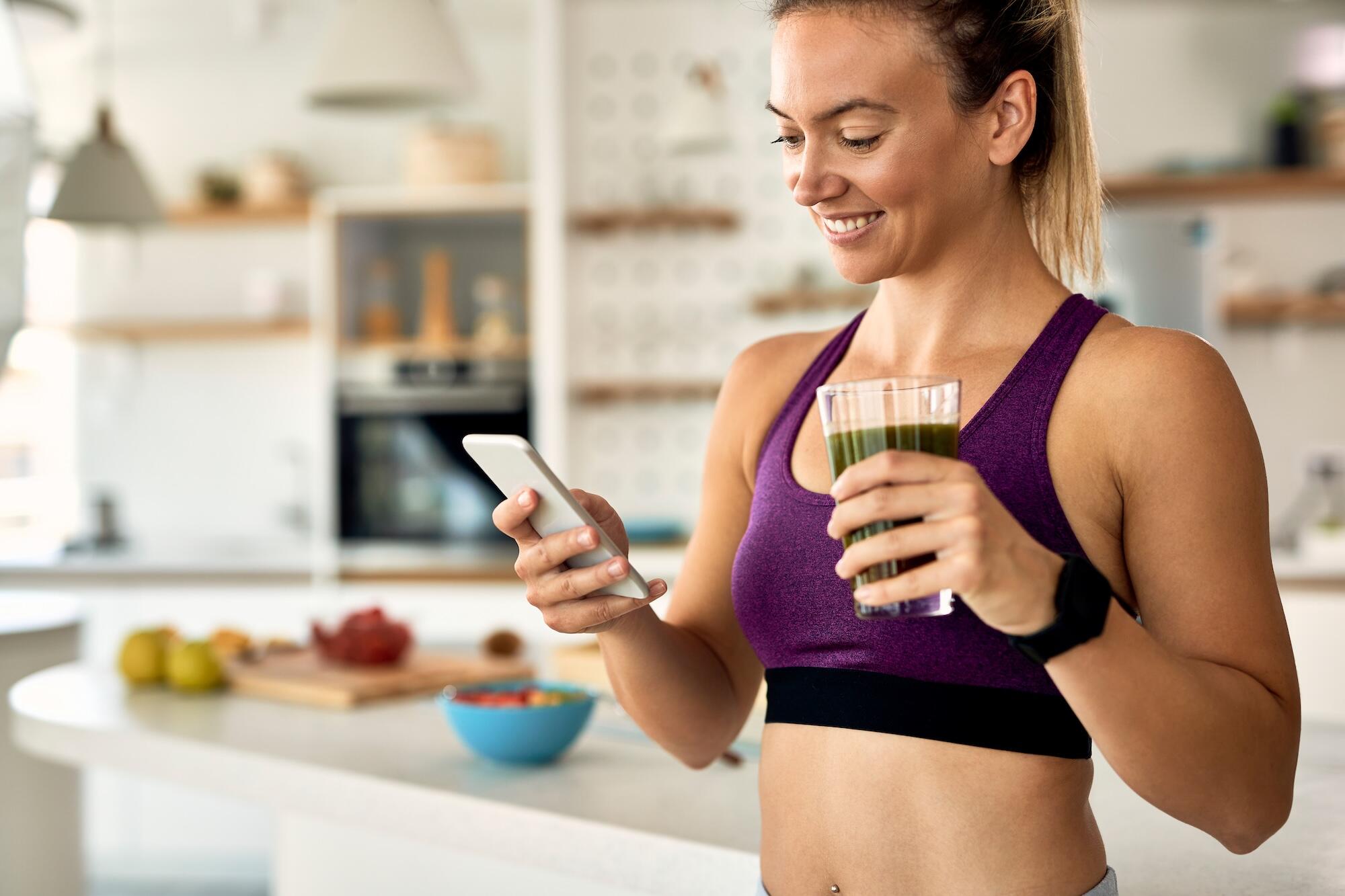 Une jeune femme regarde son portable et tient un smoothie dans sa main.