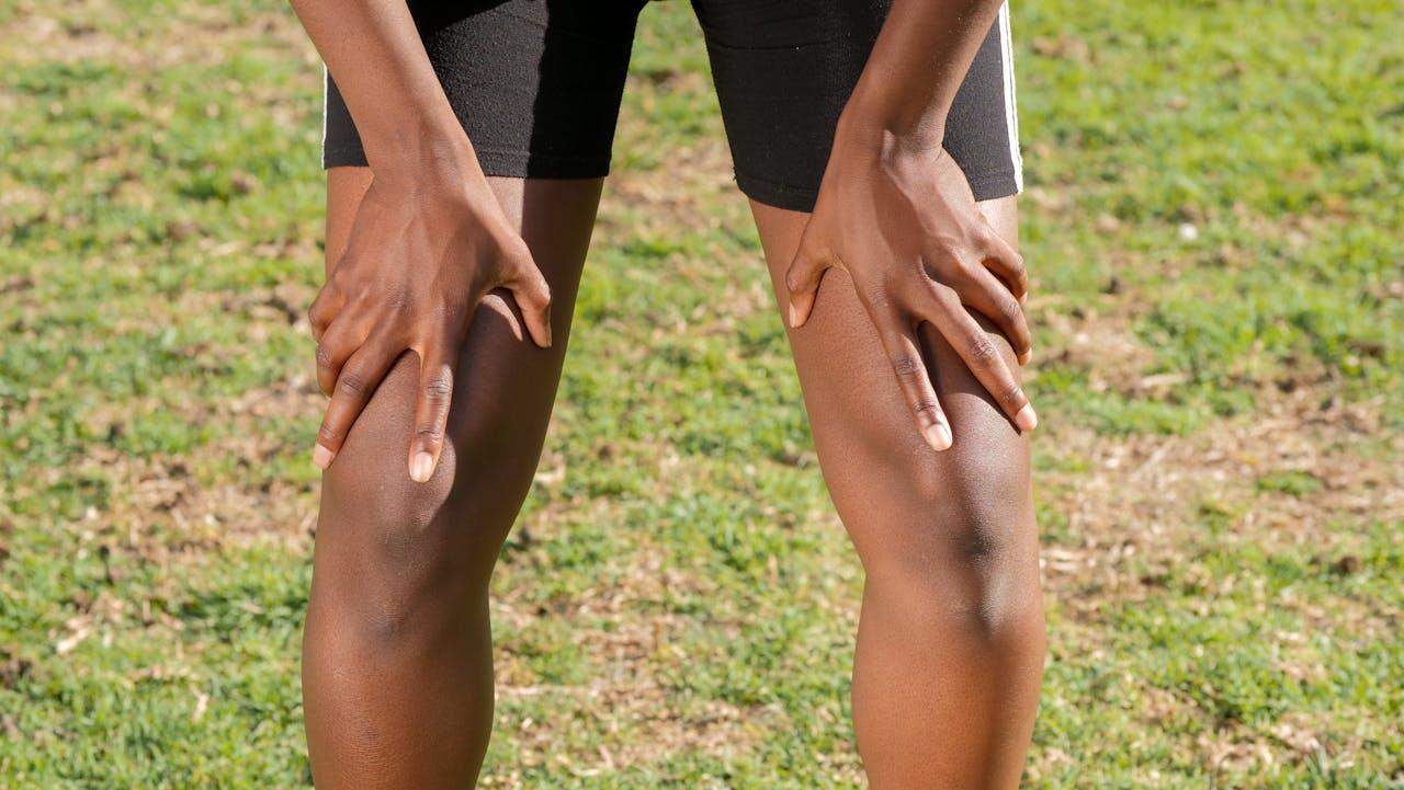 Homme noir se penchant en avant avec les mains posées sur ses cuisses. Il porte un short noir et on ne voit que le bas de son corps.