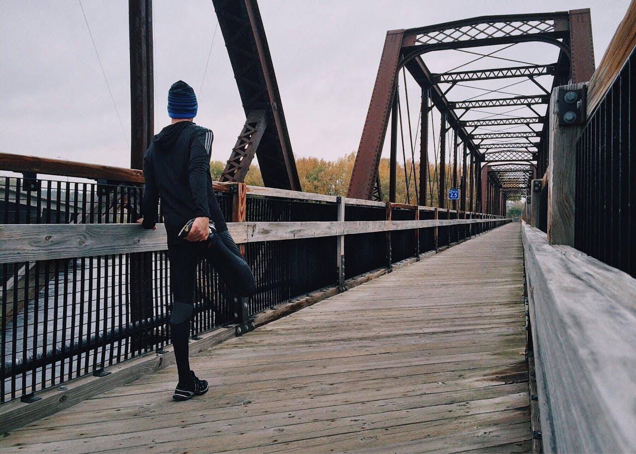 Jeune homme s'étirant le quadriceps sur un pont.