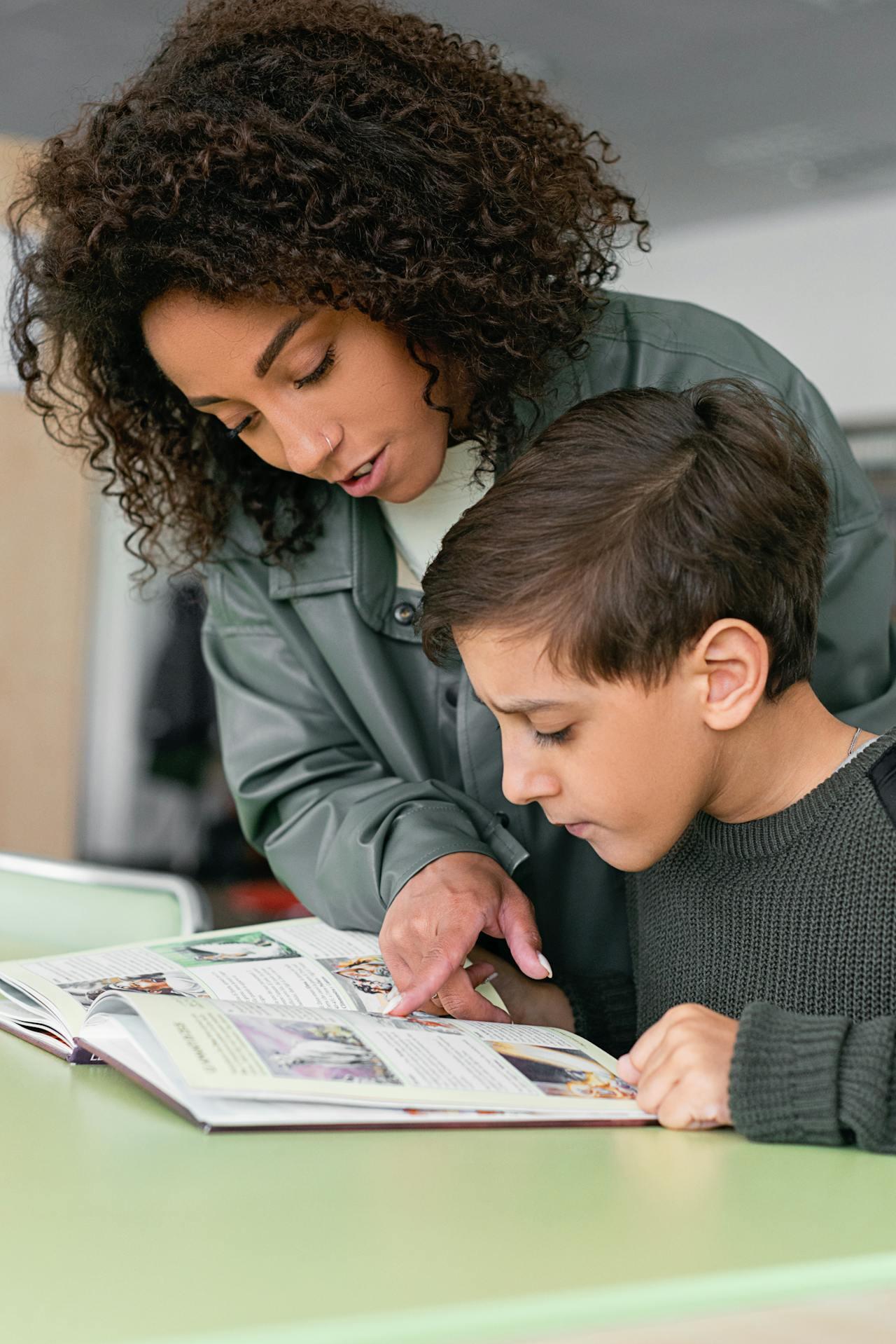 Jeune professeure aidant un élève à lire un texte dans un livre.
