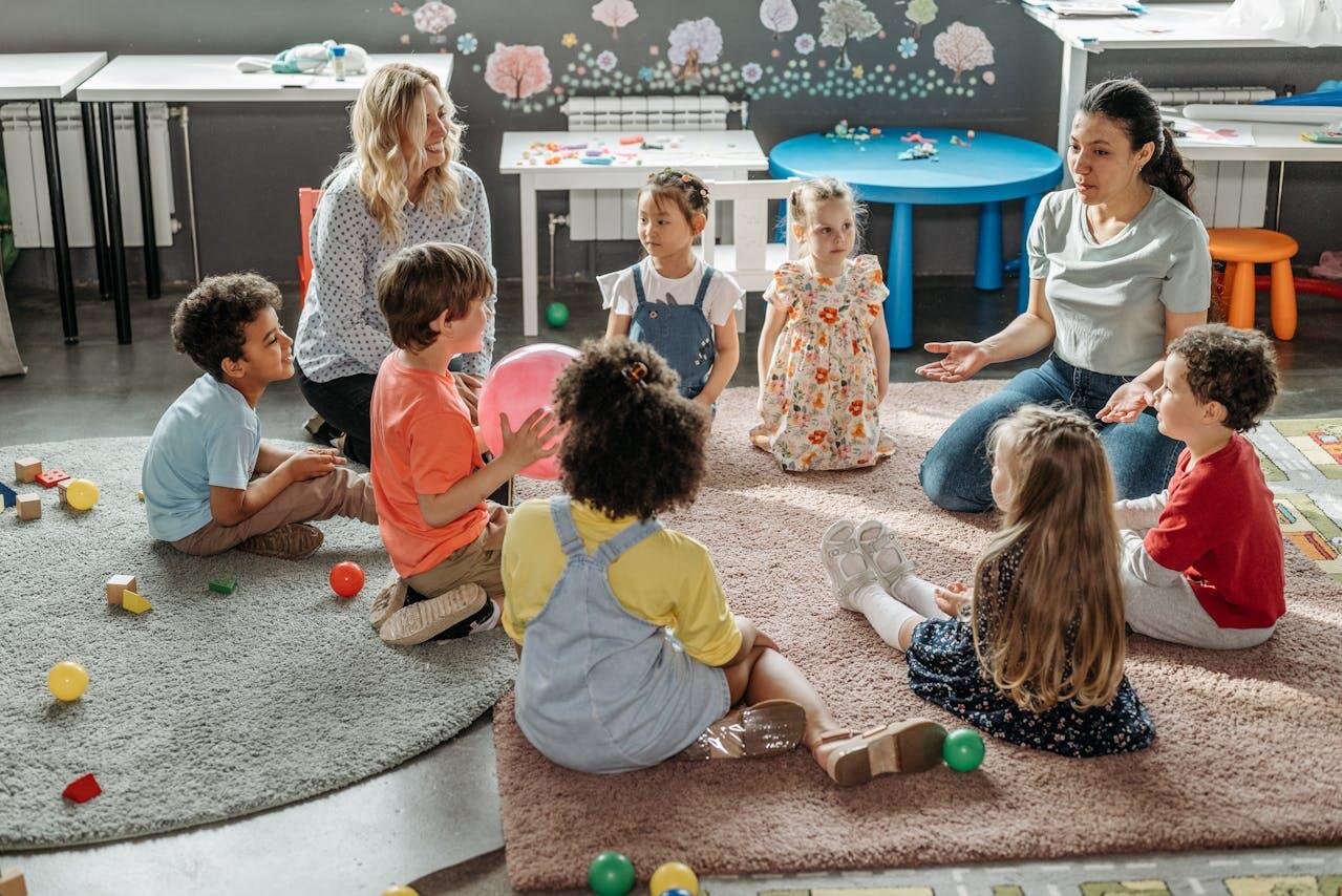 Deux femmes entourées d'enfants assis par terre à l'école.