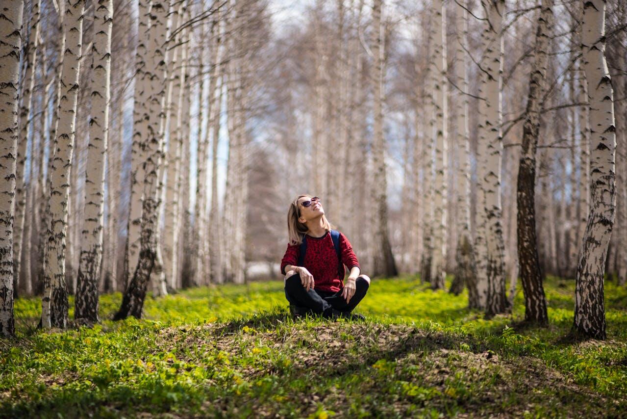 Jeune femme assise en tailleur et regardant en l'air au milieu des arbres. 