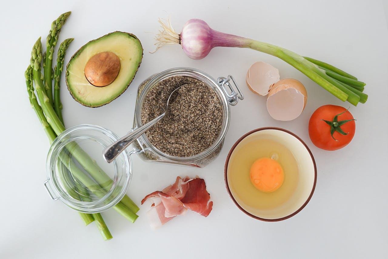 Ingrédients vus d'en haut : asperges, oeuf cassé dans un bol, tomate, oignon, avocat...