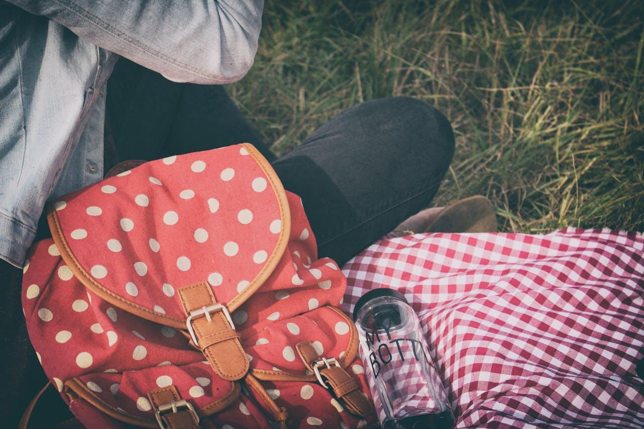 Jeune femme assise par terre avec un sac rouge à pois et une gourde en verre. 
