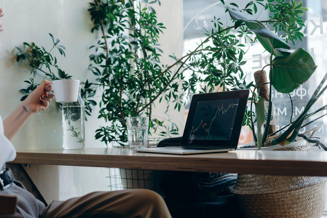 Personne assise à son bureau, devant un ordinateur portable ouvert, une tasse de café à la main. 