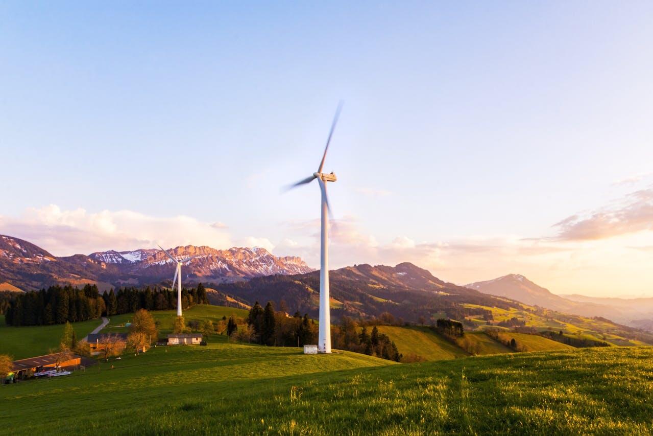 Photo de deux éoliennes en marche dans un paysage vert de montagne. 
