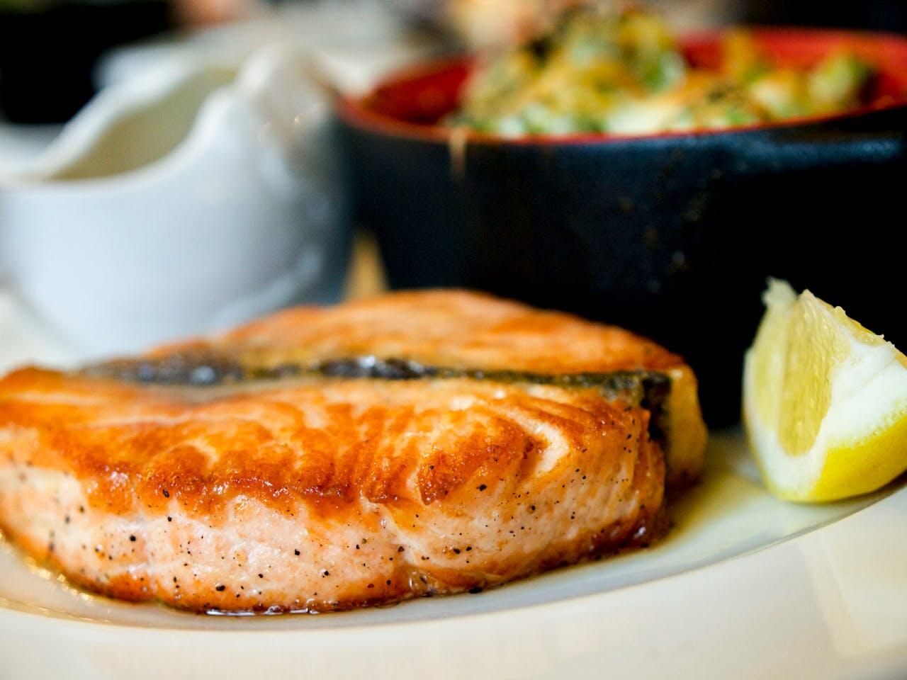 Tranche de saumon grillé avec du citron et un bol de légumes en fond. 