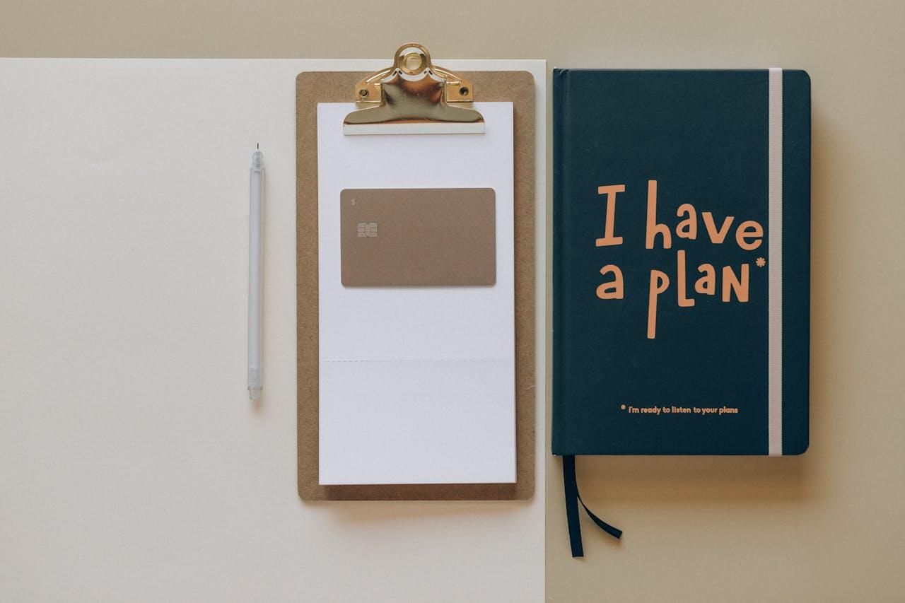 Carnet marqué "I have a plan" (j'ai un plan), une carte bancaire et un stylo. 