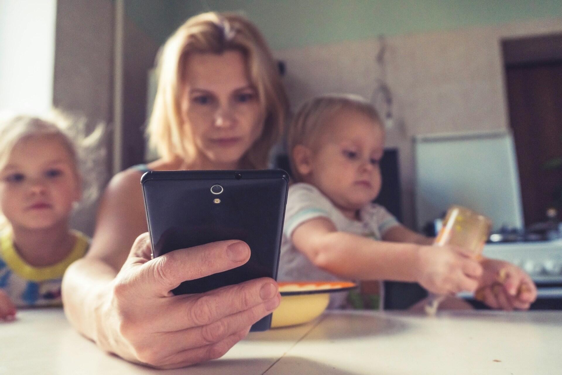 maman en train de consulter son téléphone avec ses enfants dans les bras