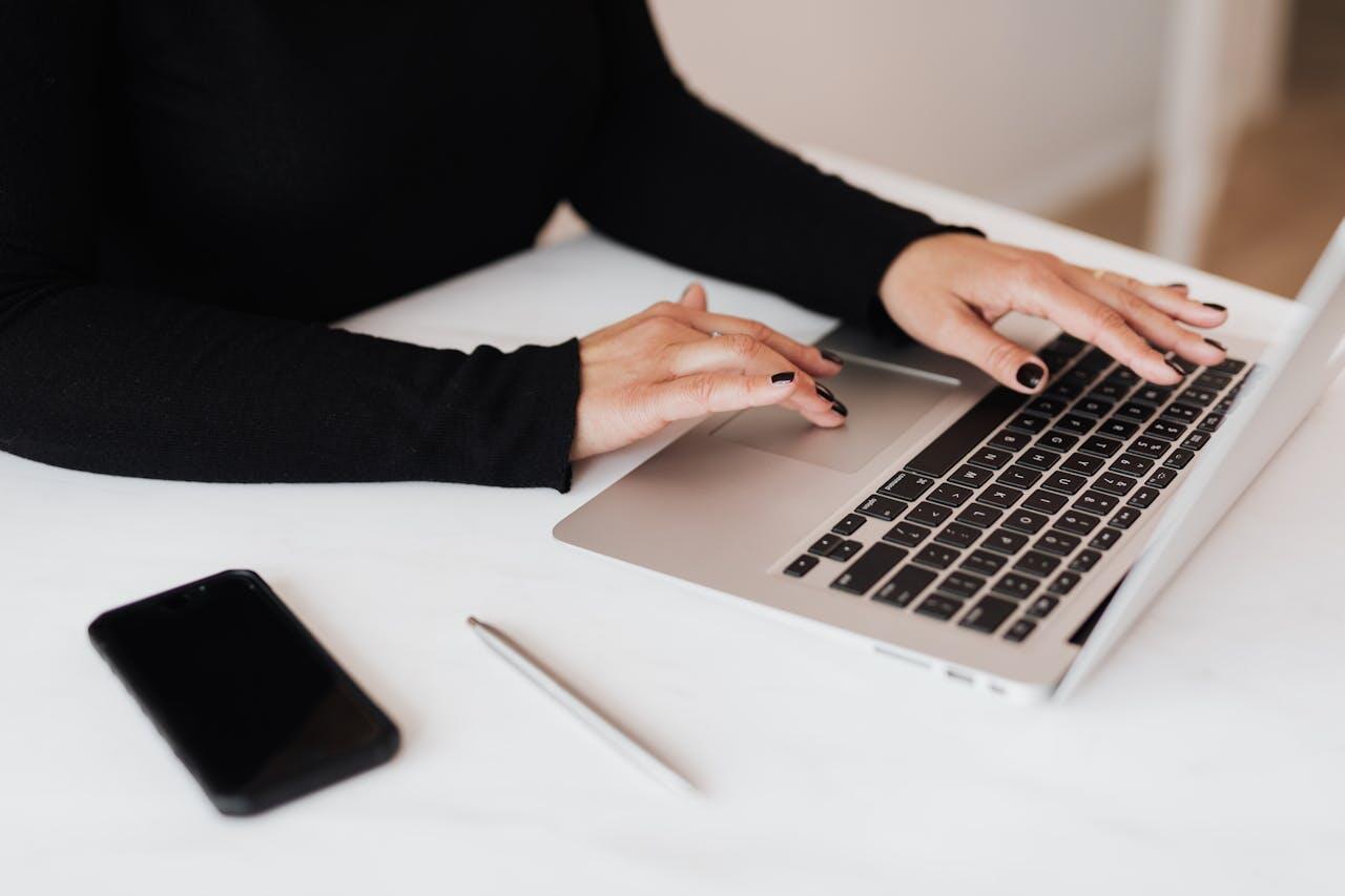femme en noir et aux mains manucurees travaillant sur son ordi avec telephone a cote