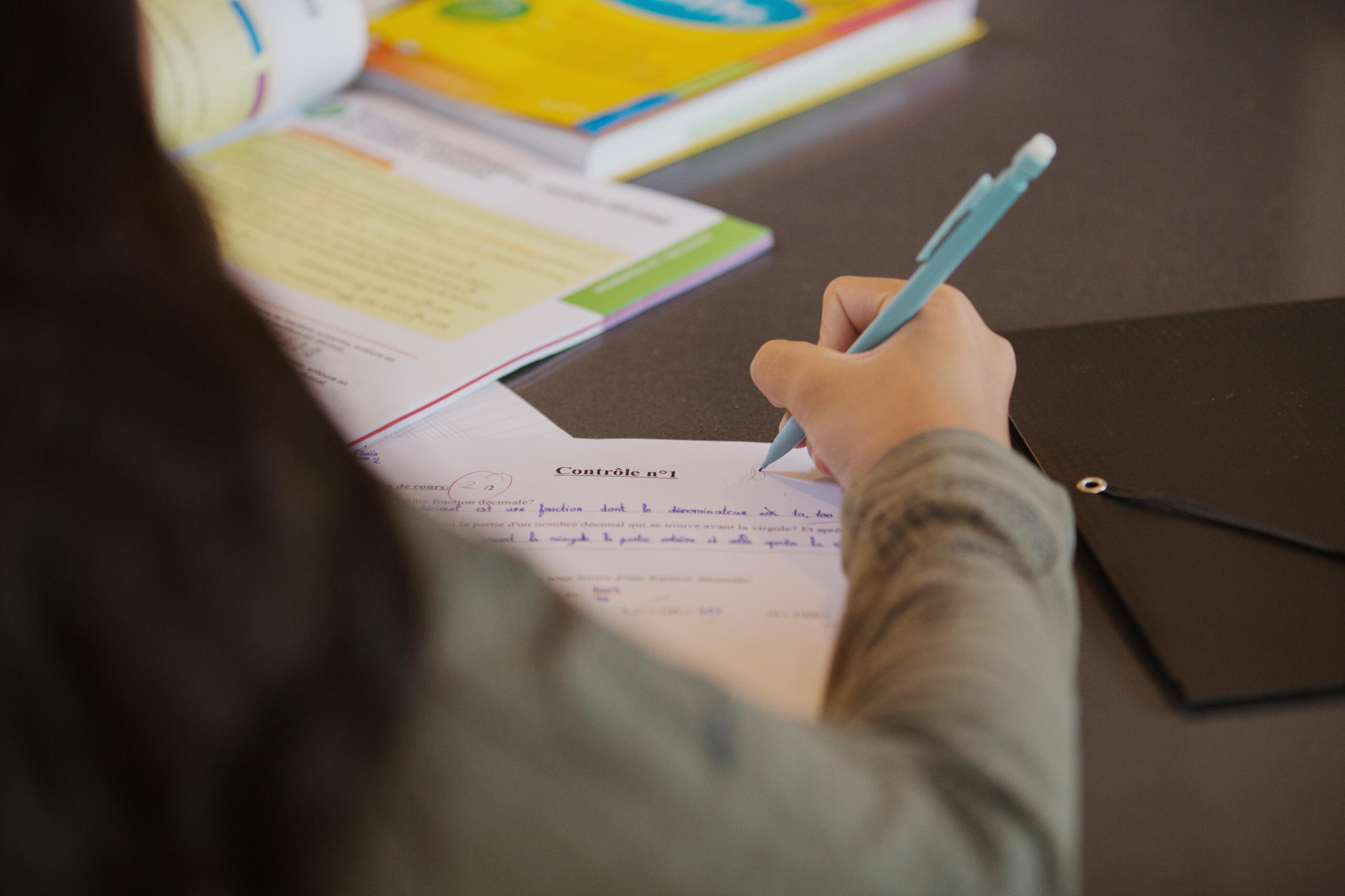 Jeune fille de dos penchée sur un contrôle de mathématiques lors d'un cours à domicile.
