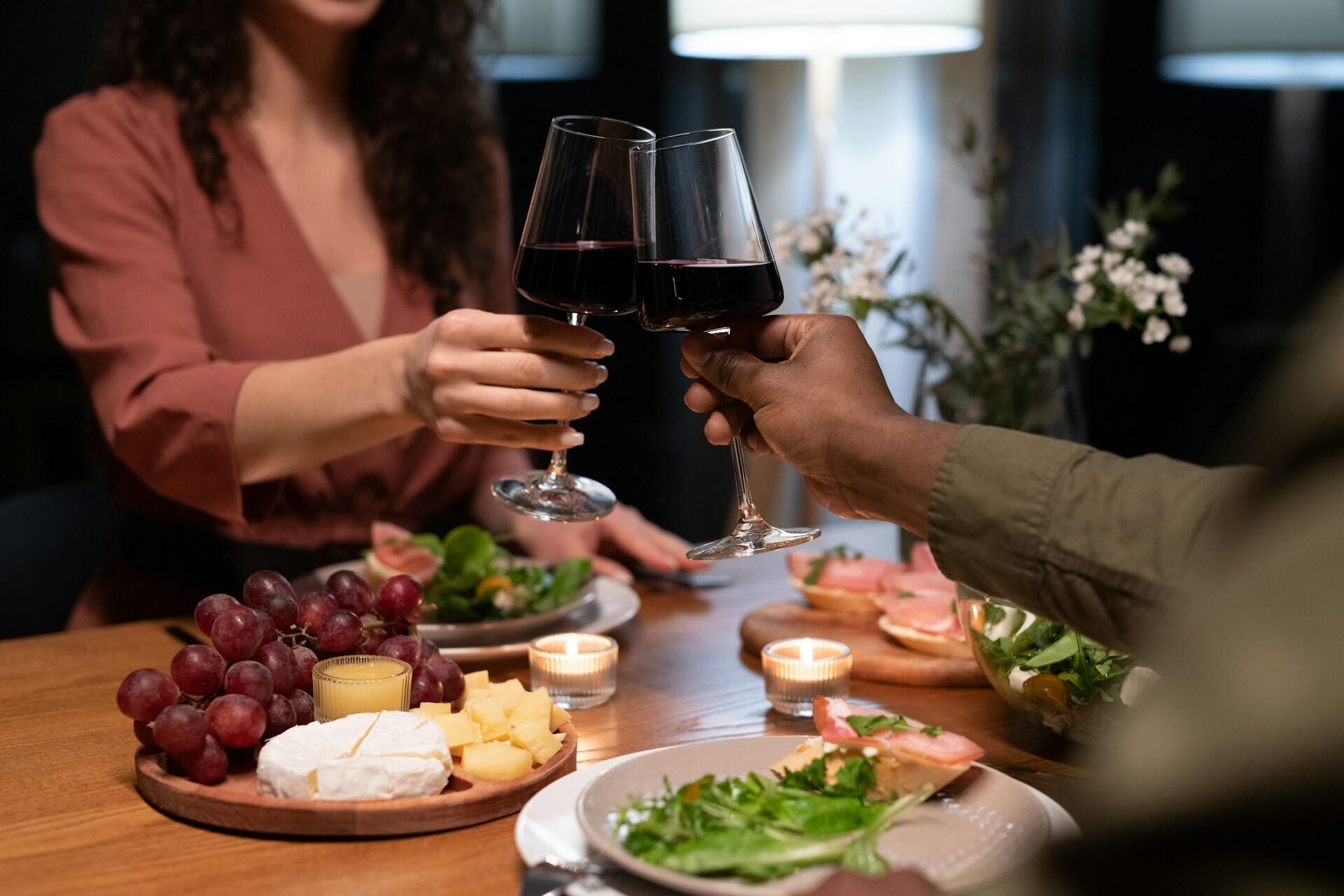 Deux personnes qui dînent et qui trinquent avec leur verre de vin rouge