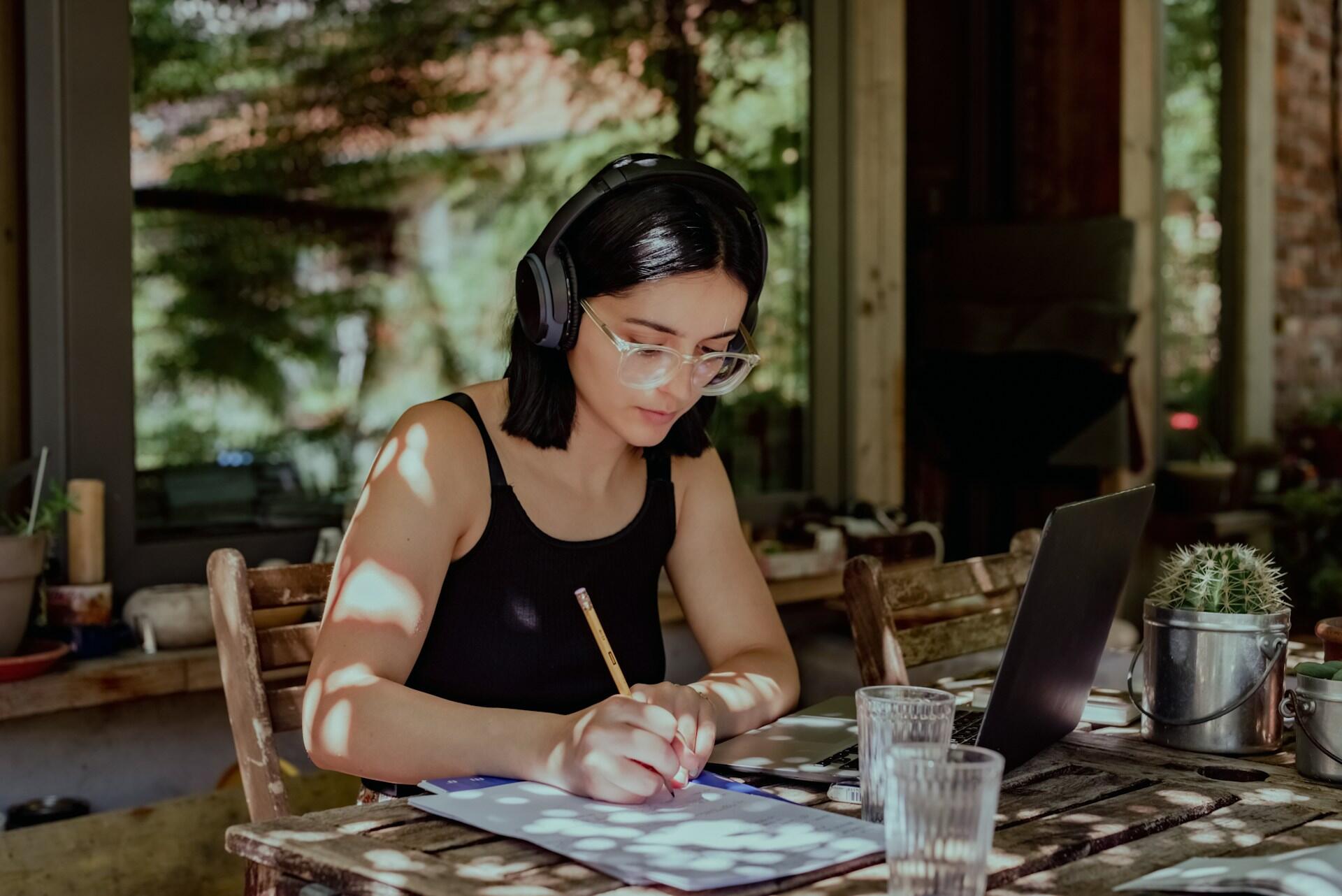 Une femme avec un casque audio qui écrit sur un carnet sur une terrasse