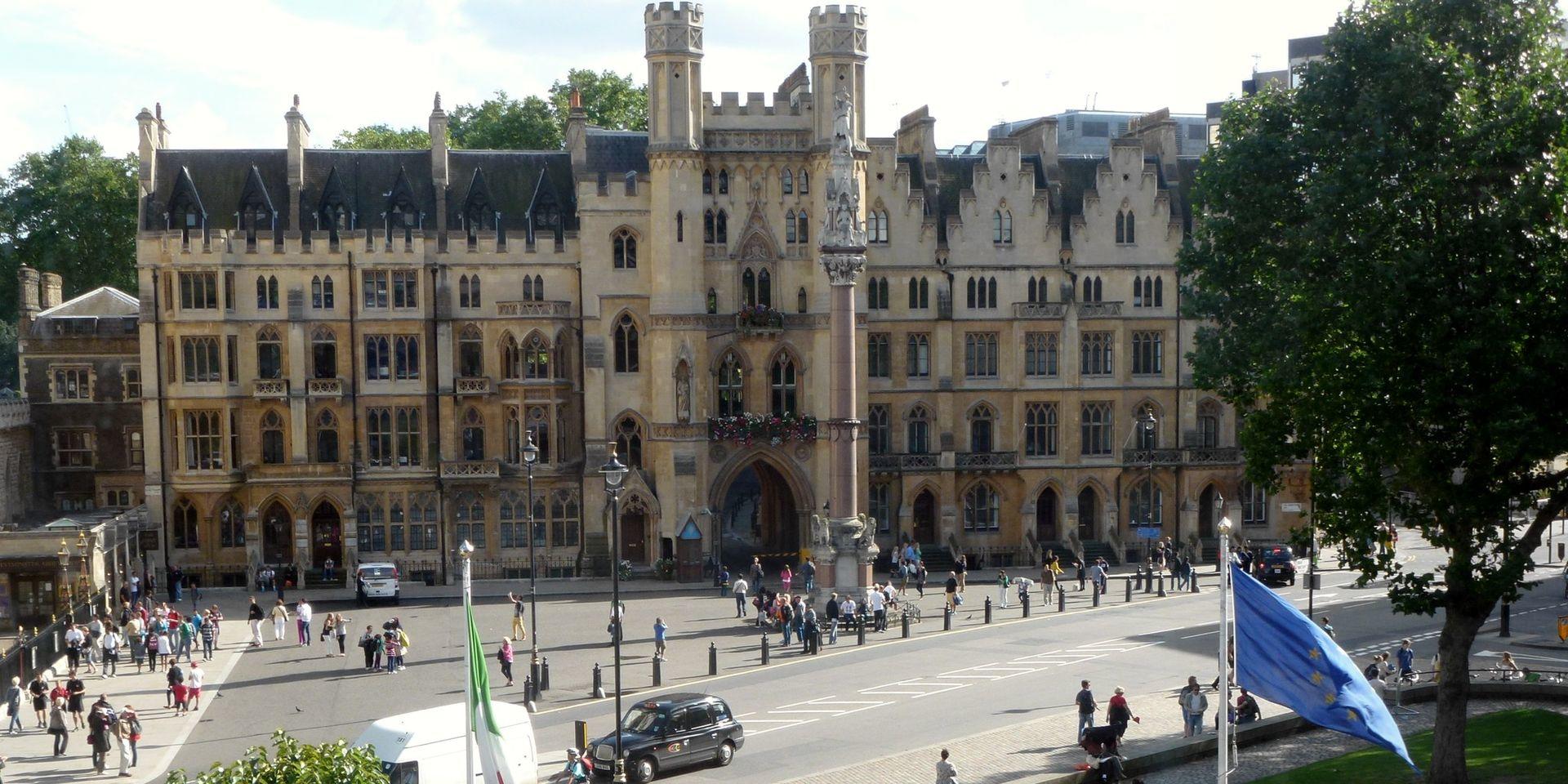 The entrance to Dean's Yard and Westminster School war memorial with people mingling on the sidewalk and a taxi on the road.