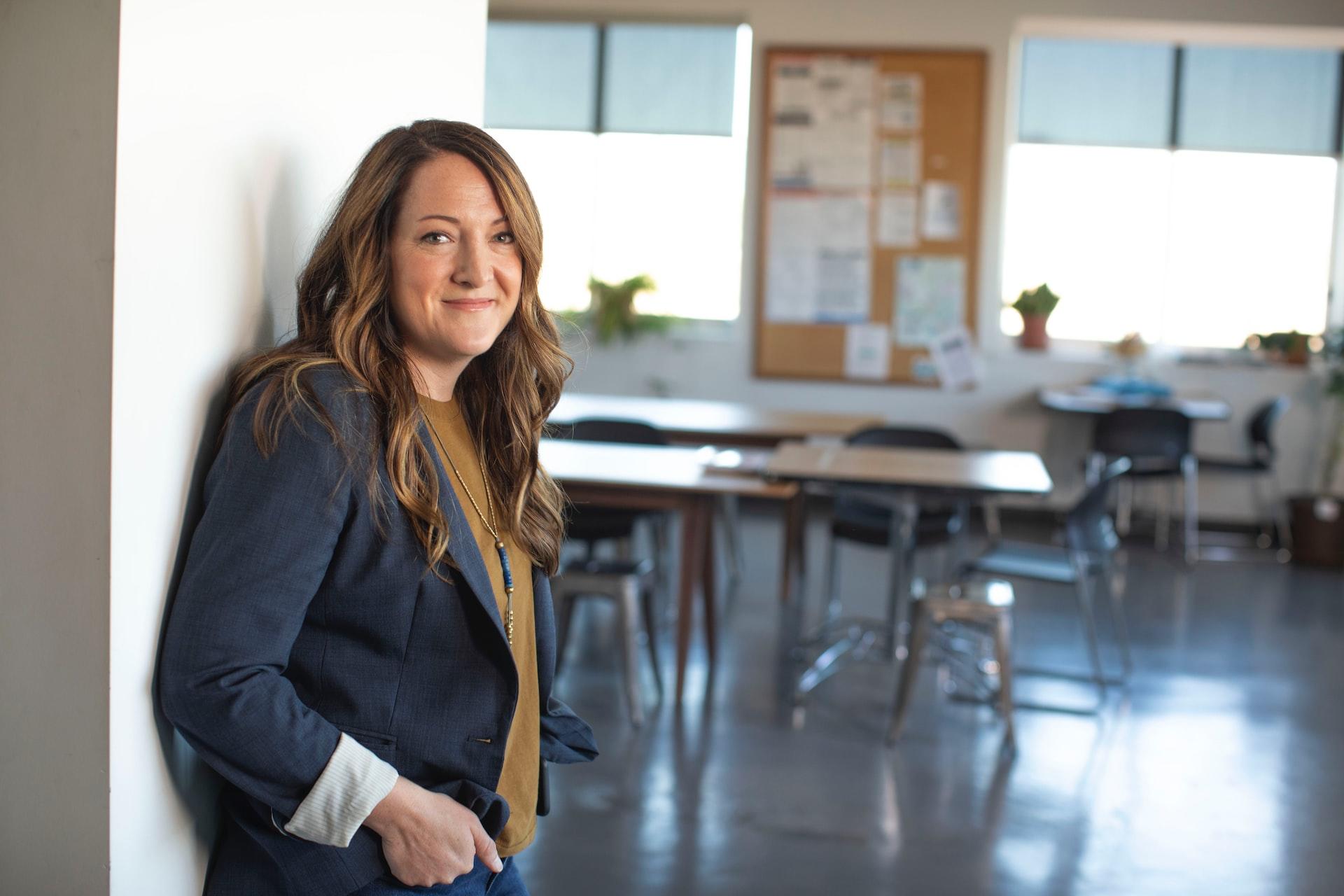 A woman in a grey blazer stands in the doorway to a classroom. 