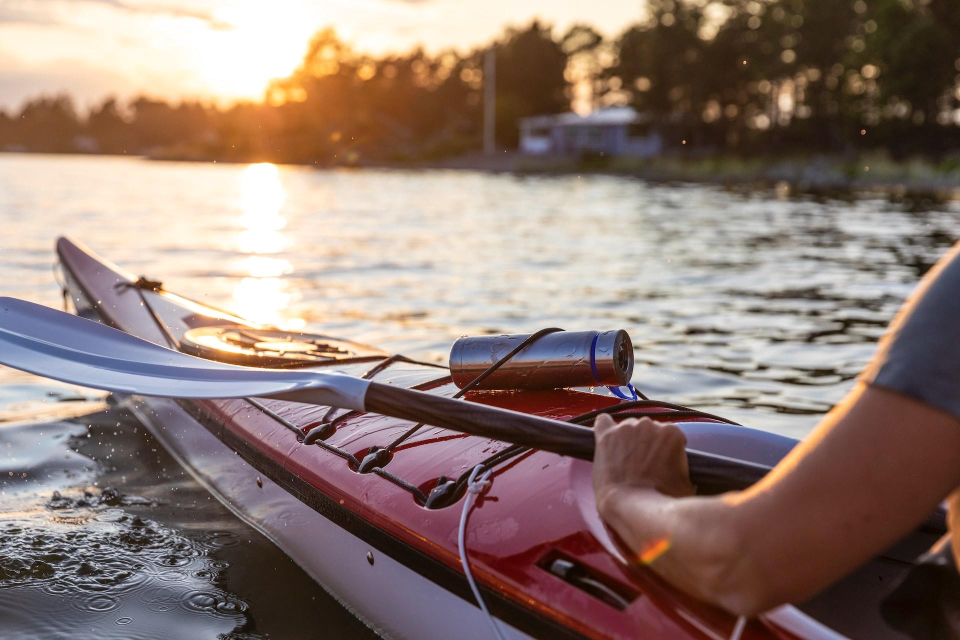 A red kayak on the water at sunset with a metal flask attached to its tie-downs