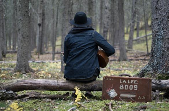 A man practicing guitar in the woods