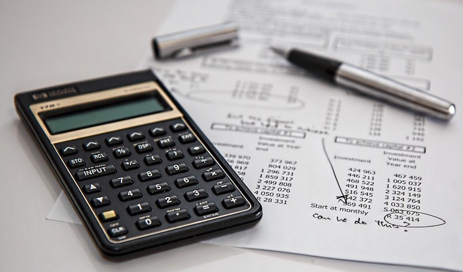 A black-case calculator with gold trim sits next to an uncapped silver pen which, in turn, lies atop an expenses sheet.  