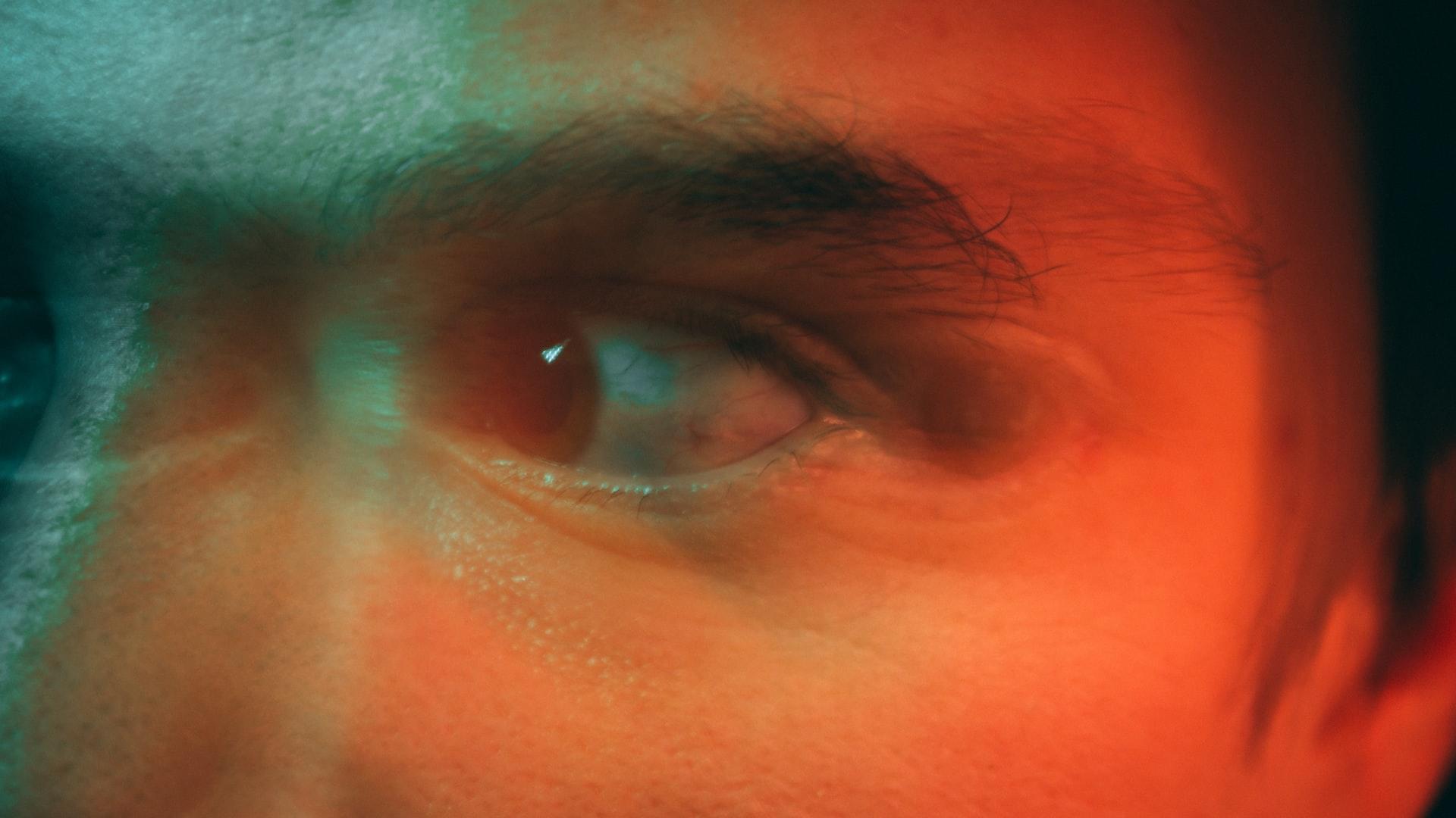 A closeup of a man's eyes looking to the right in a malicious manner, with an orange filter and a blur applied. 