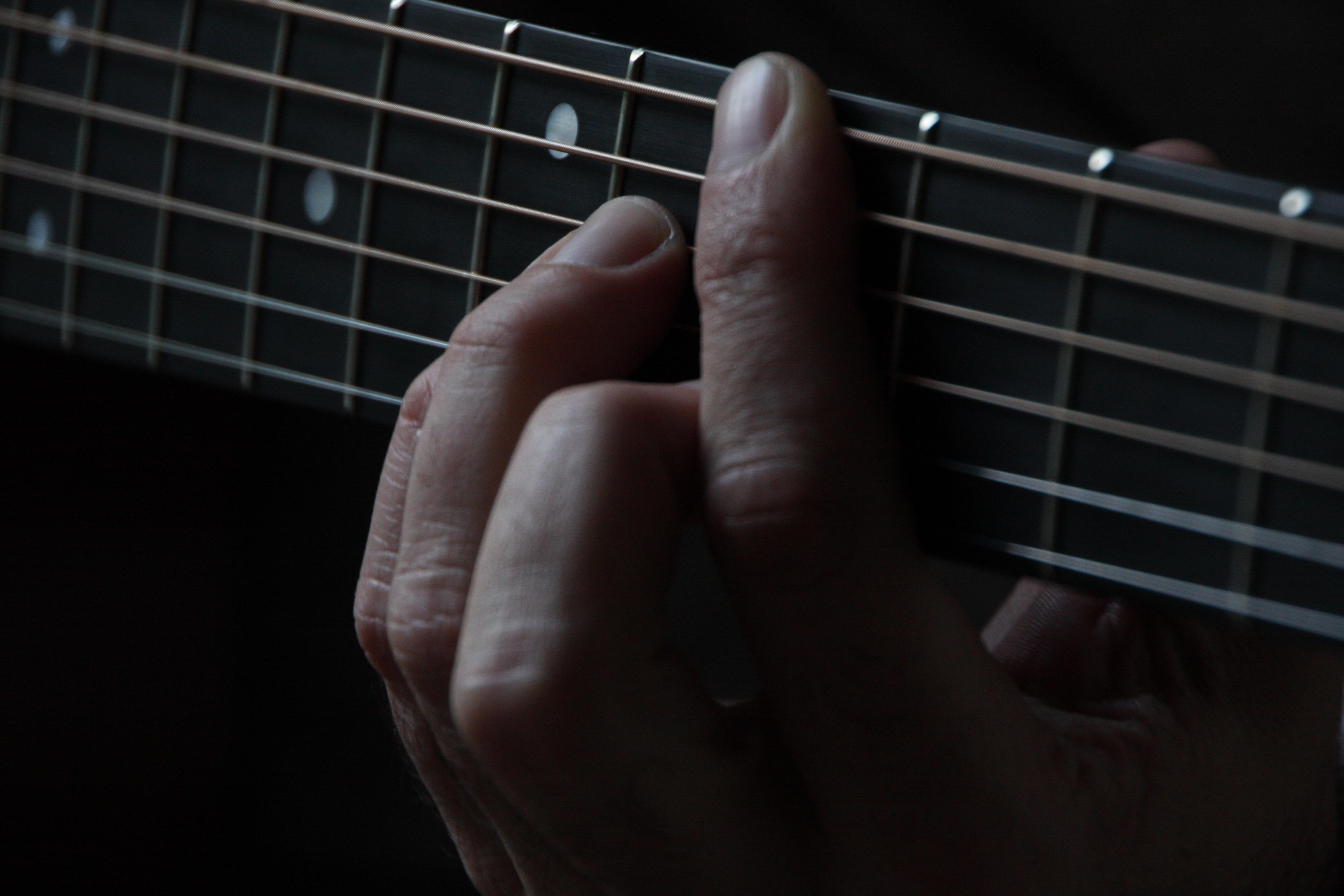 a dark photo of someone playing a chord on a guitar.