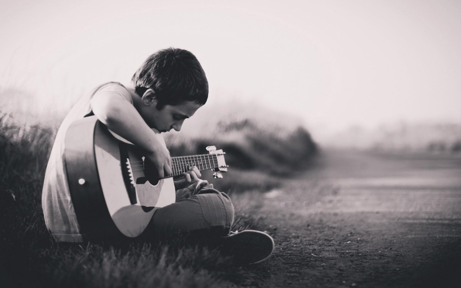 A boy practices how to play the guitar.