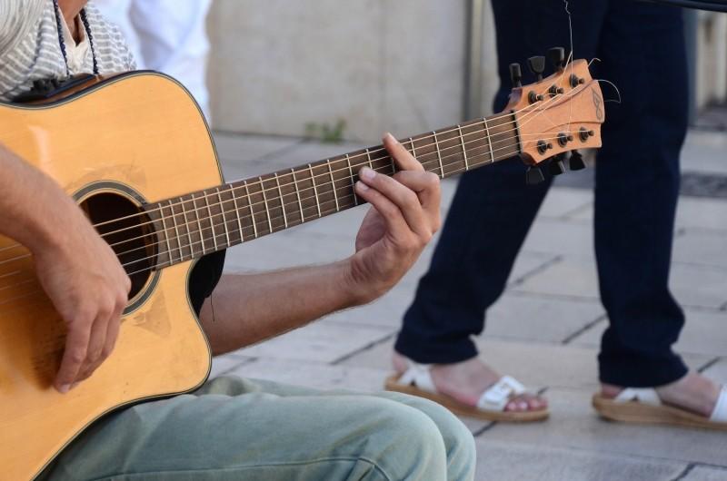 Busker plays guitar on street.