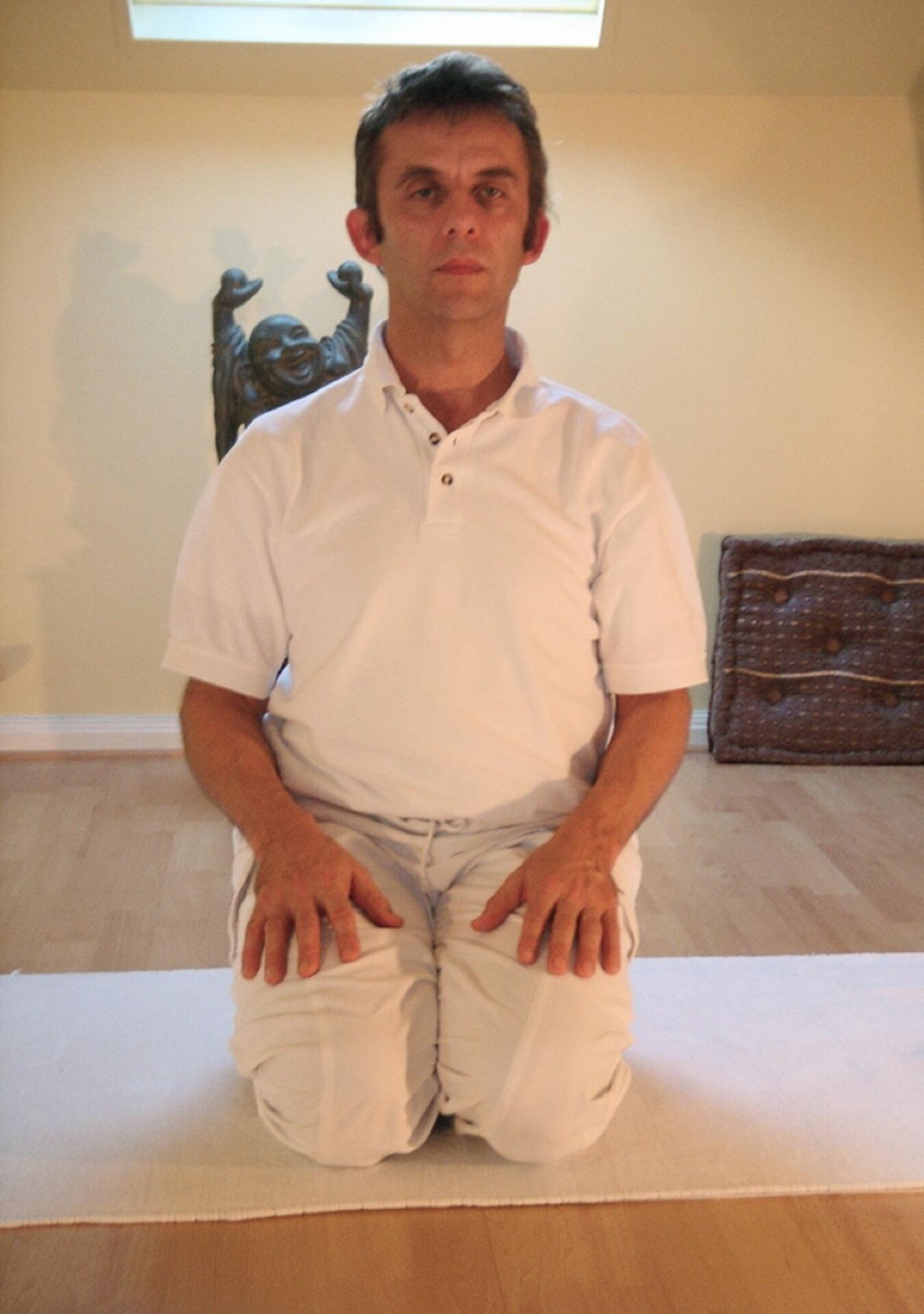 A man wearing white kneeling with hands on thighs.