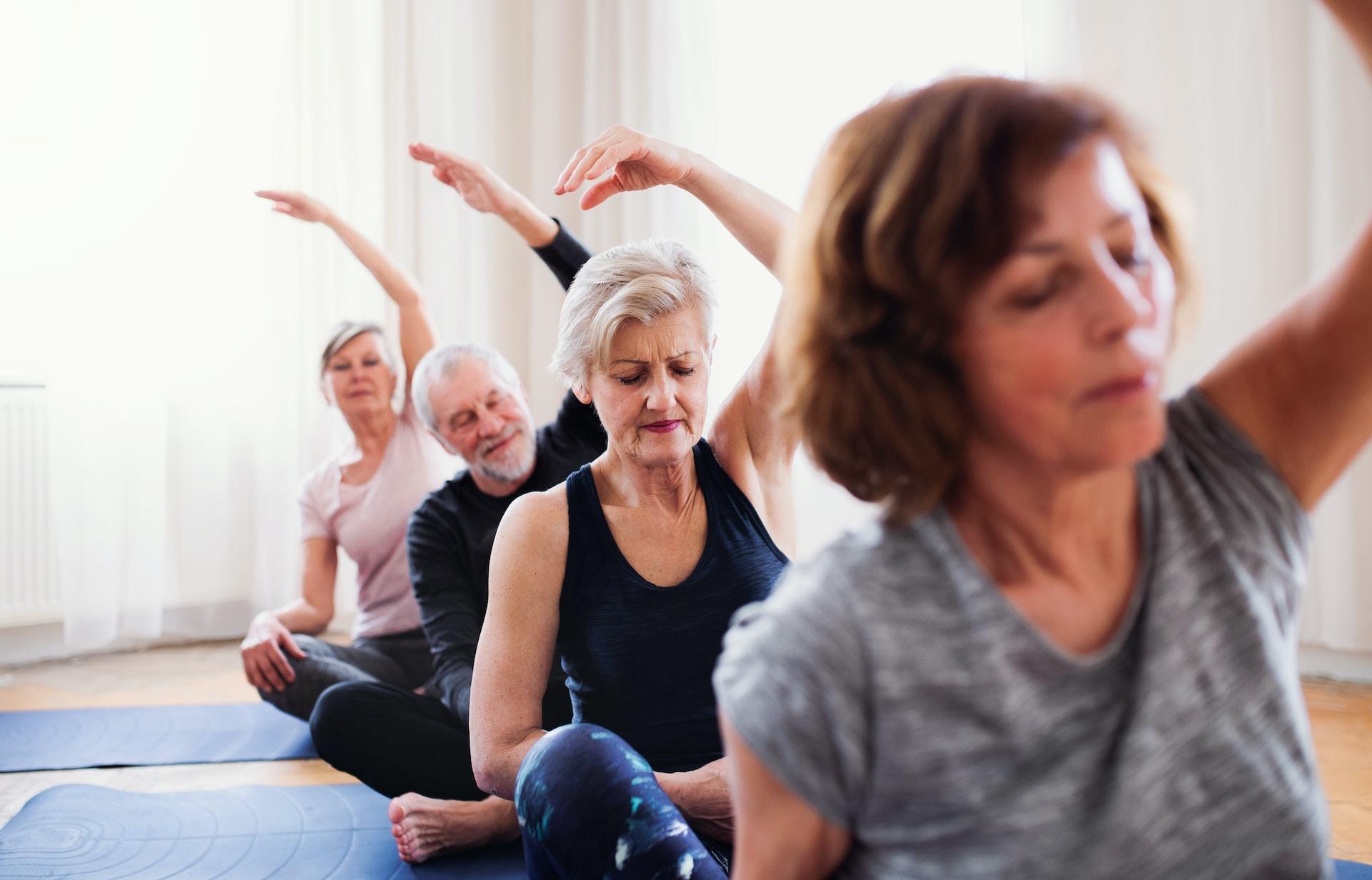 Four elderly people are sitting in a row doing yoga.