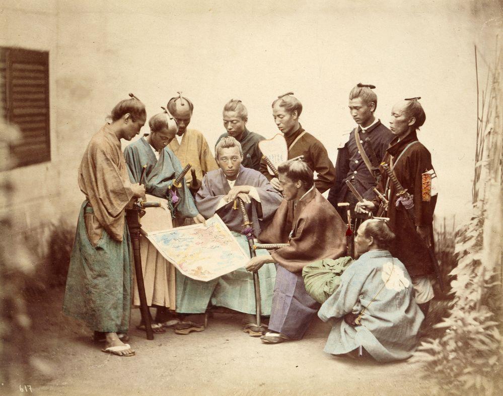 A group of eight individuals in traditional Japanese attire gathers around a colorful map.