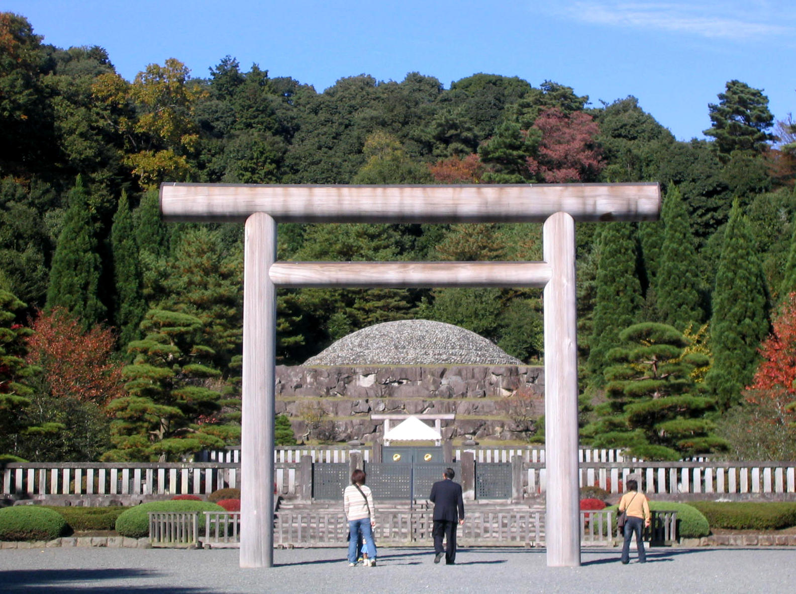 A Shinto shrine prefacing a burial mound of Emperor Hirohito, seen against a background of green with a clear blue sky above. 