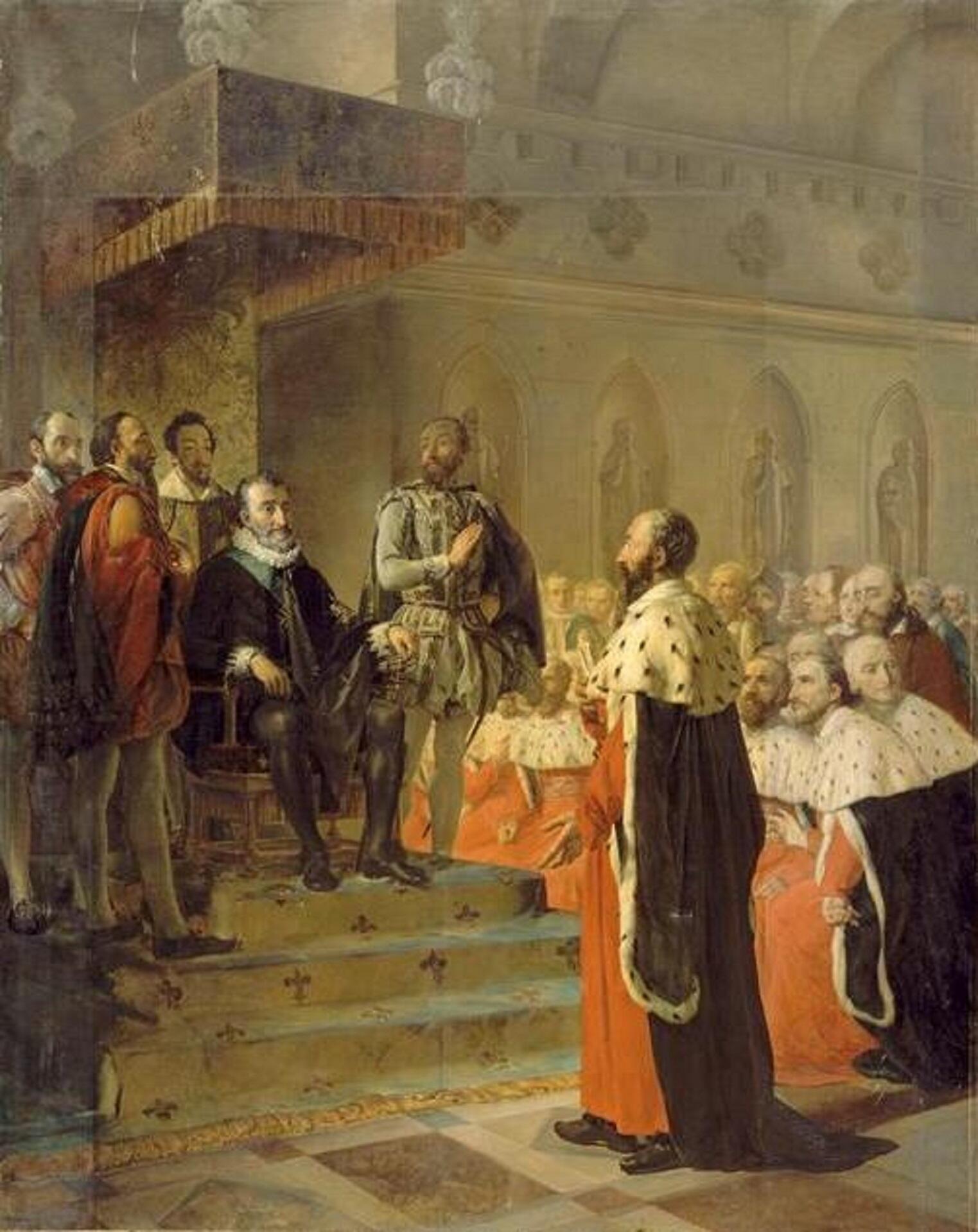 A man sits on a dais with others surrounding him, while another man stands in front of him.