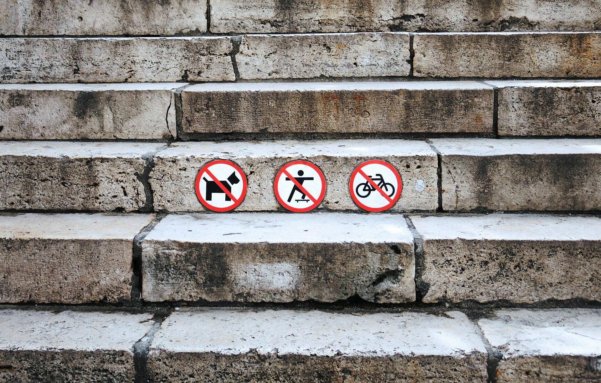 Three round signs forbidding activities on a stone staircase.