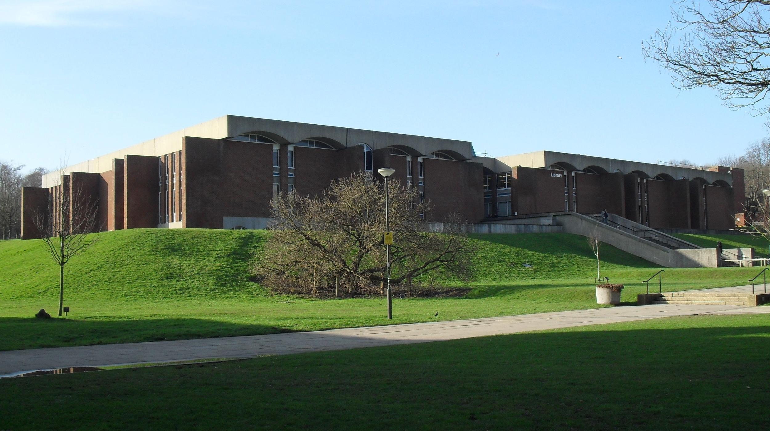The University of Sussex library on a sunny day, it's brick and concrete structure sitting atop a small knoll. 