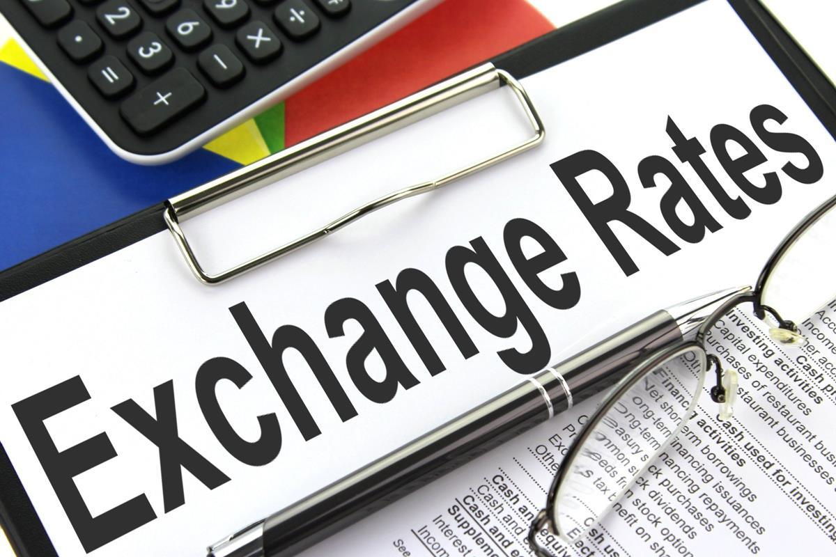 A sign that has "exchange rates" written on it, next to a calculator, a pair of glasses, and some paperwork. Exchange rates were controlled at one point in the post war period through the Bretton Woods system.