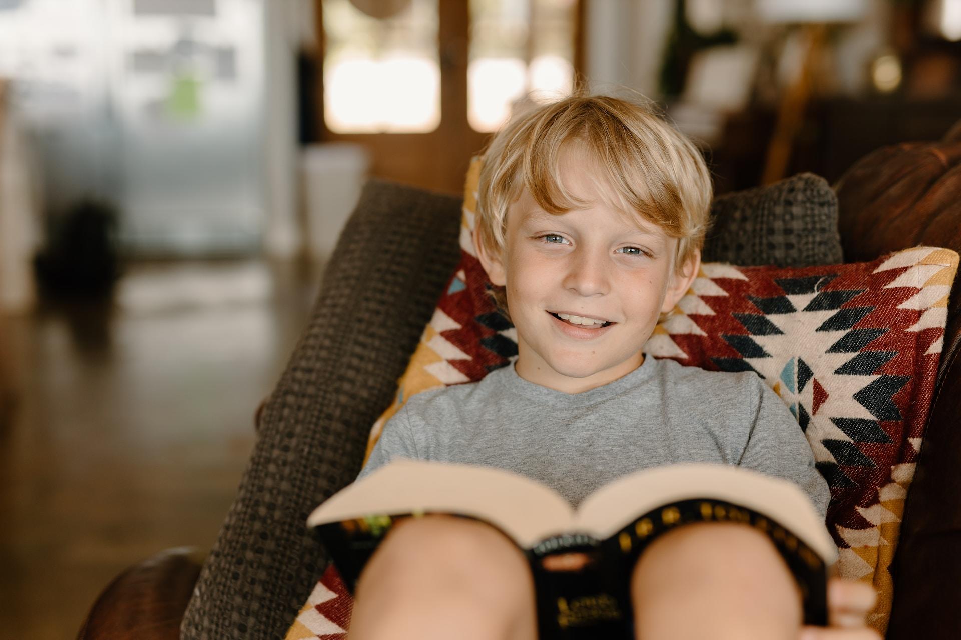 A boy sitting in a sofa eith a book in his hand.
