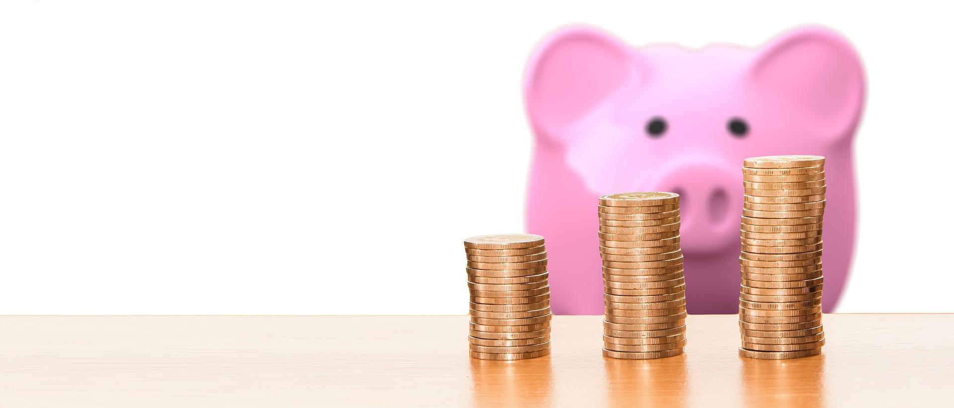 An image of three stacks of gold coins in ascending height with a pink piggy bank placed behind them. The image is off-centre, towards the right. Knowing your budget can help you control the cost of Portuguese lessons.