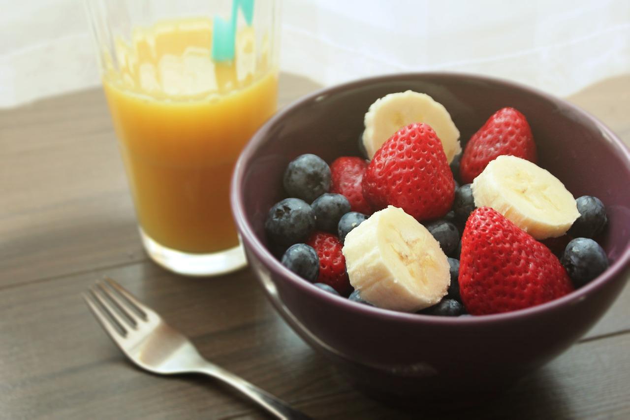 A healthy diet includes breakfast, as shown here. The image contains a glass of orange juice, a fruit bowl, and a fork.